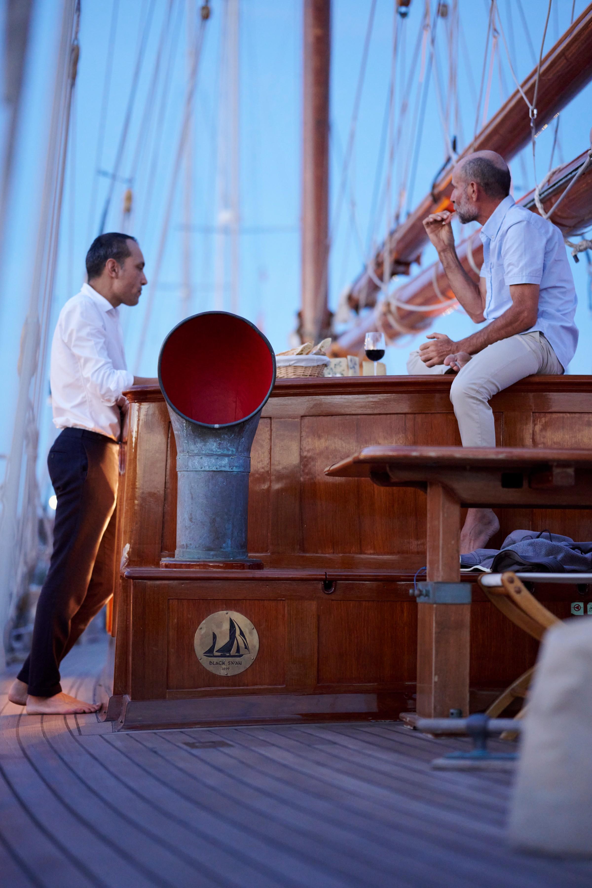 Two guests sharing wine and cheese board on the teak deck of classic sailing yacht Black Swan at dusk