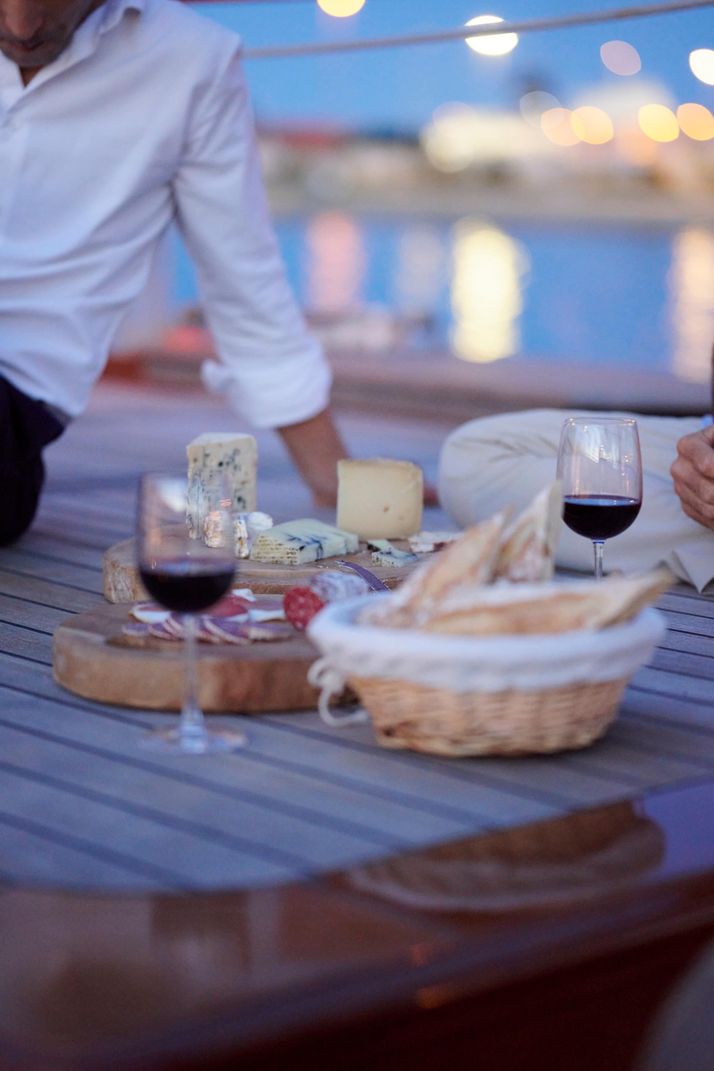 luxury gulet deck dining with cheese board, charcuterie, bread basket and red wine at dusk