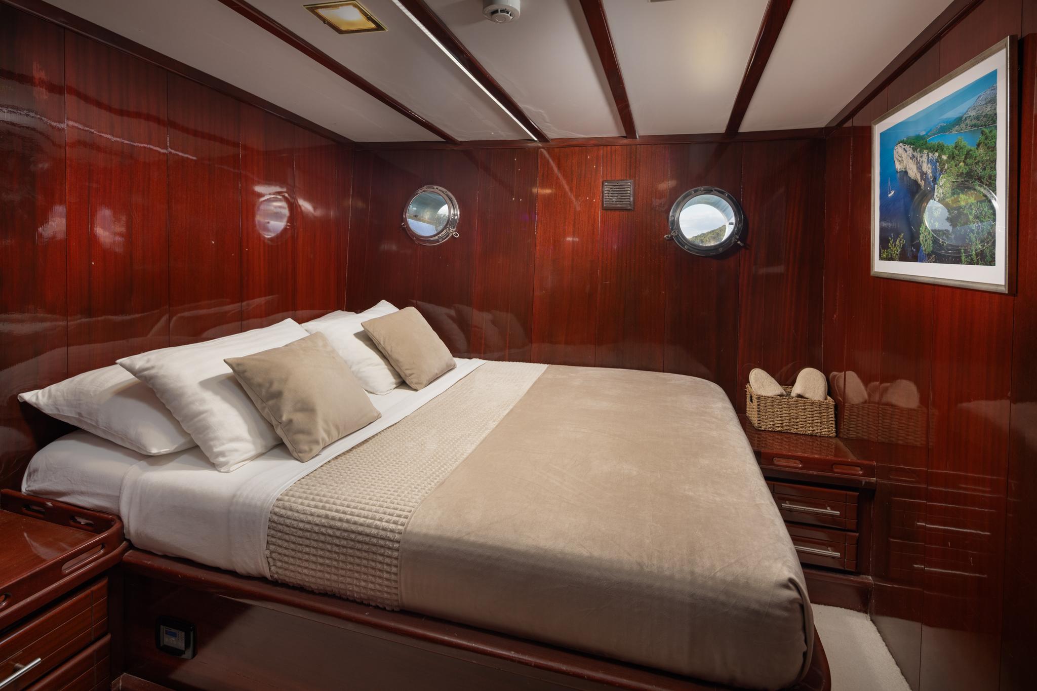 yacht guest cabin with double bed, rich wood paneling and round portholes