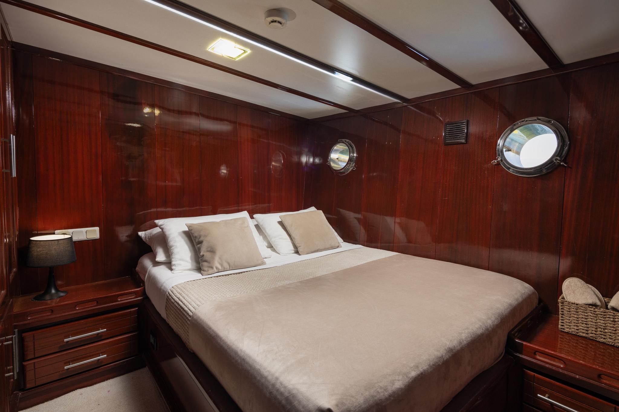 yacht cabin interior with double bed, mahogany paneling and circular portholes
