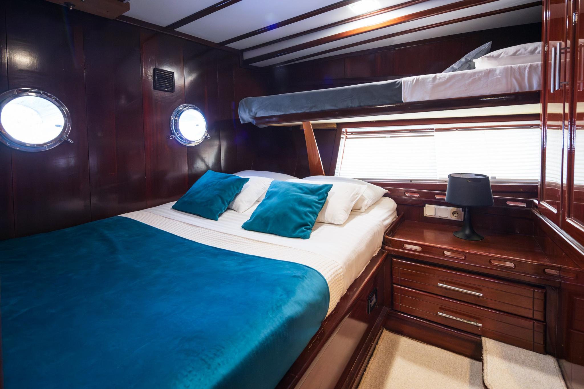 yacht guest cabin with double bed, upper bunk, portholes and wooden cabinetry