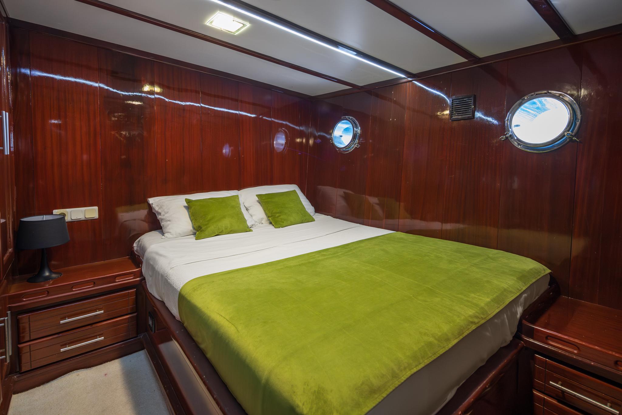 yacht guest cabin with double bed, green throw and pillows, portholes and wood paneling