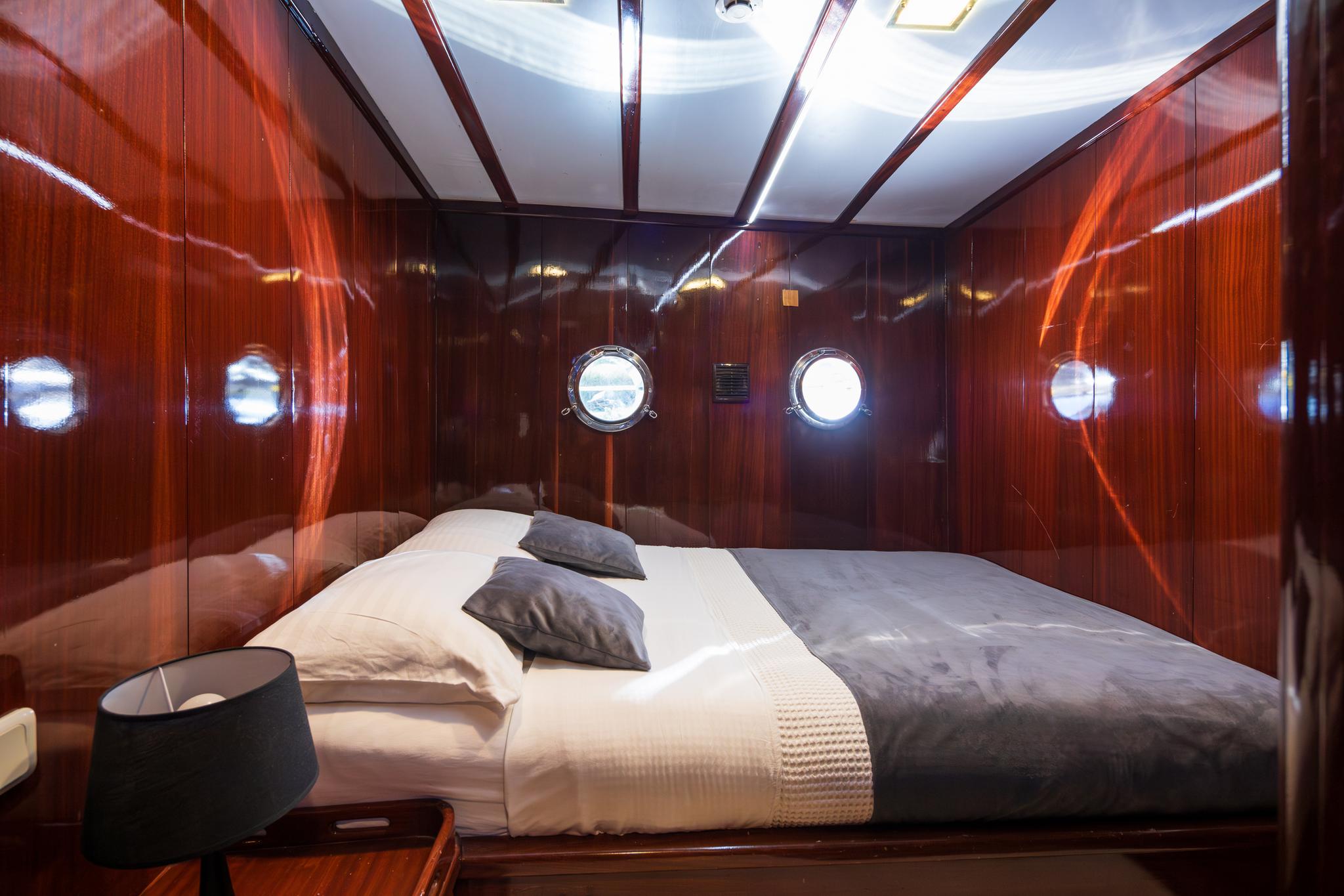 yacht guest cabin with double bed, high-gloss wood paneling and round portholes