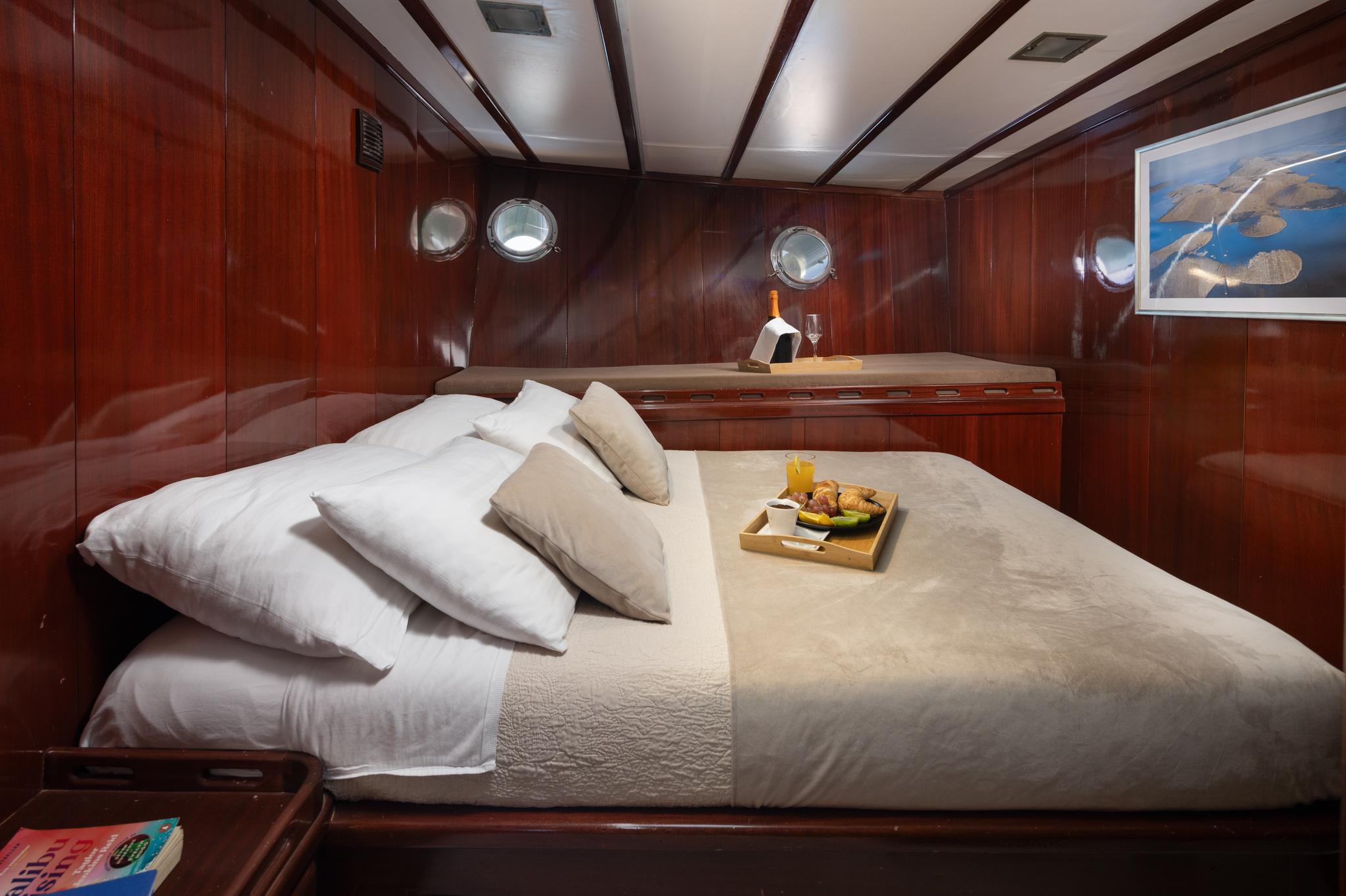 yacht guest cabin with double bed, rich mahogany paneling, portholes, and breakfast service tray