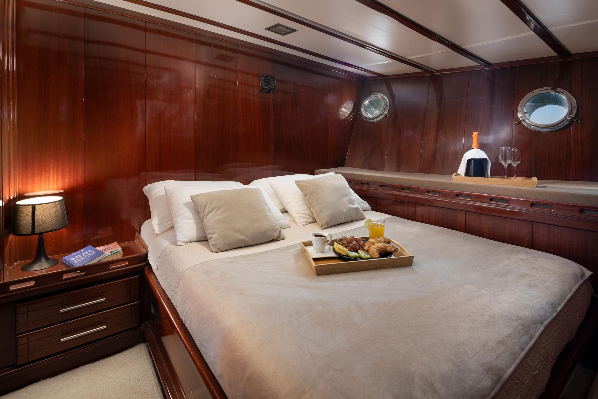 yacht cabin interior with double bed, wooden paneling, portholes and breakfast service