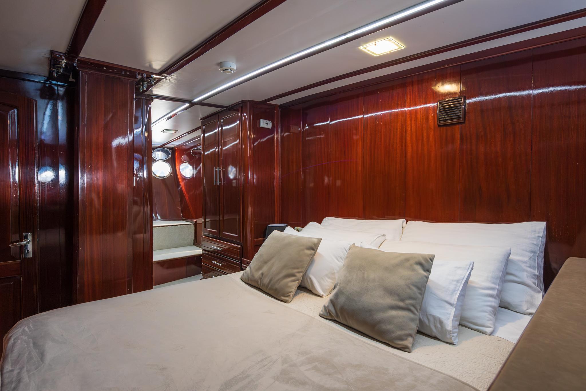 yacht cabin interior with white bedding, mahogany wood paneling and built-in storage