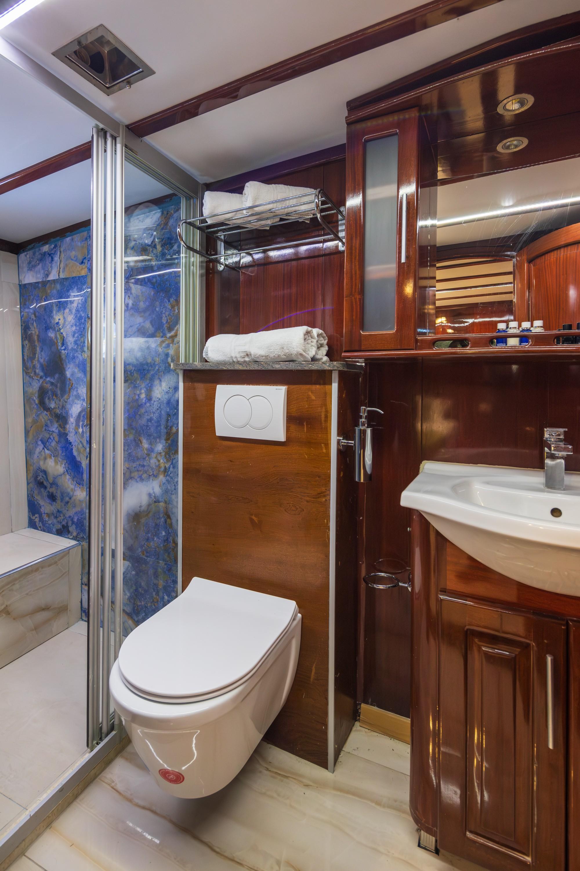 compact yacht bathroom featuring glass shower, wall-mounted toilet, wooden vanity with white basin