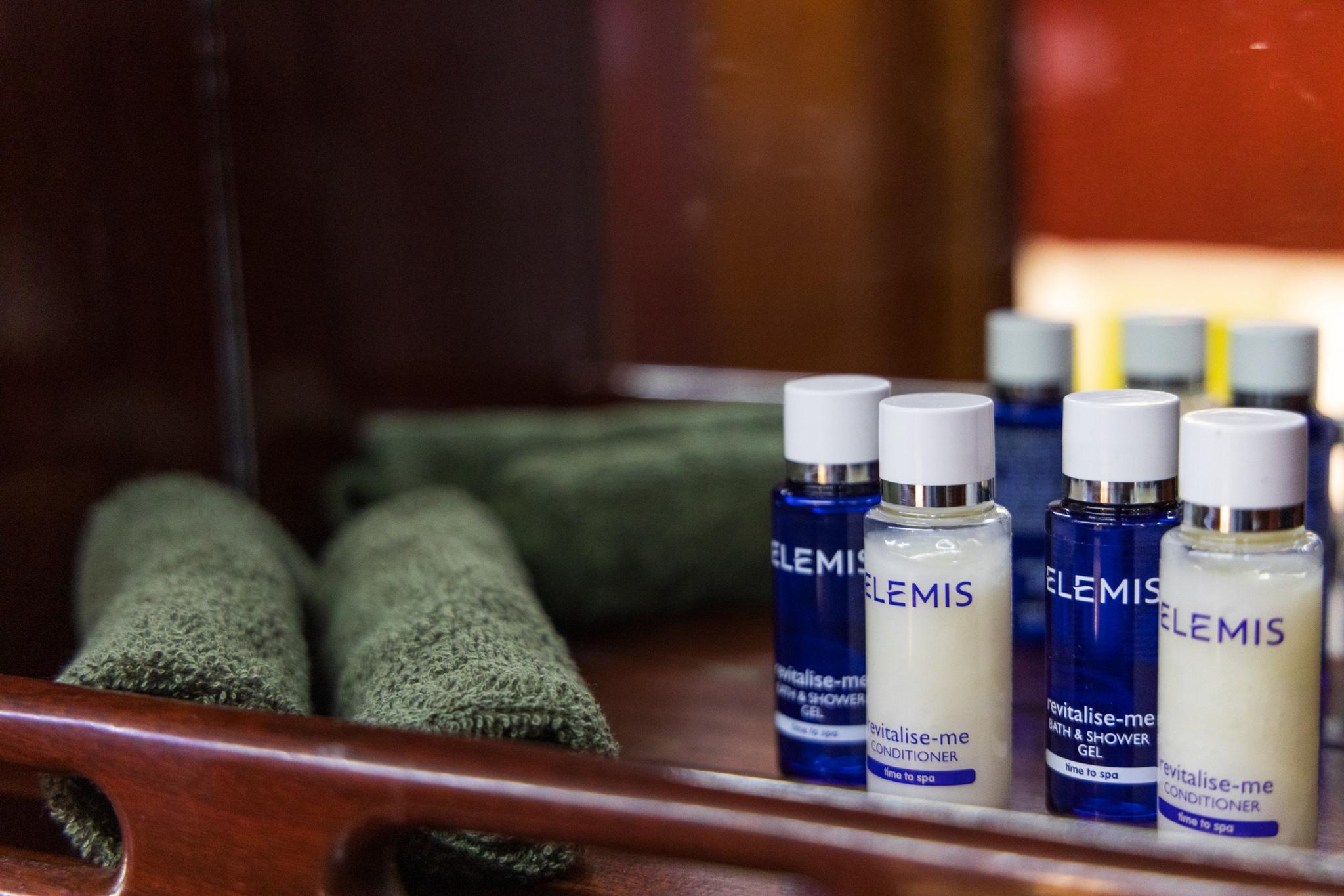 yacht bathroom with Elemis spa toiletries bottles and green towels on wooden shelf