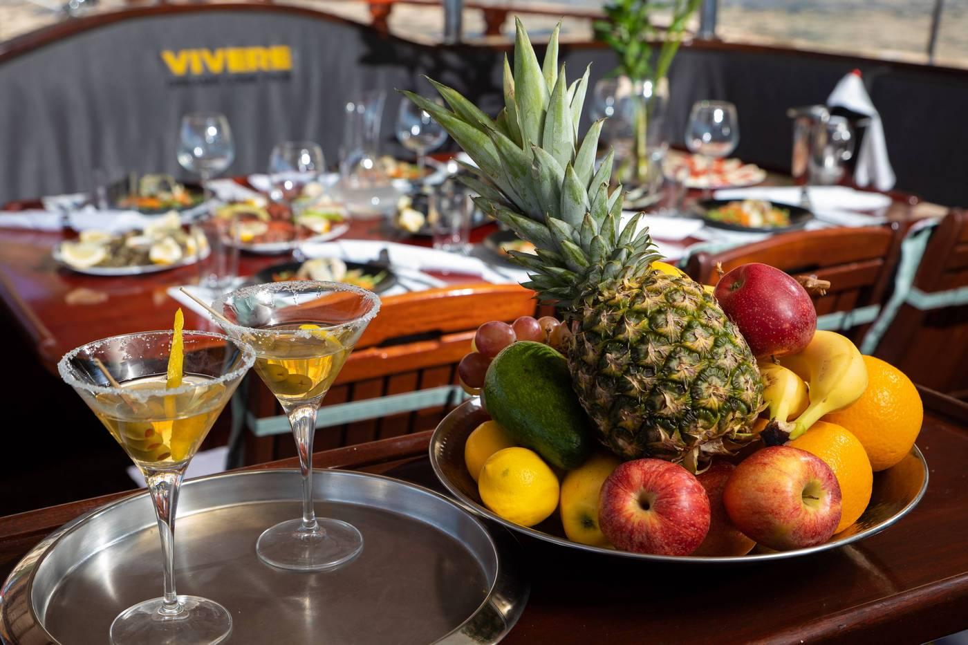 two martini cocktails with fresh fruit platter featuring pineapple and apples on yacht dining table