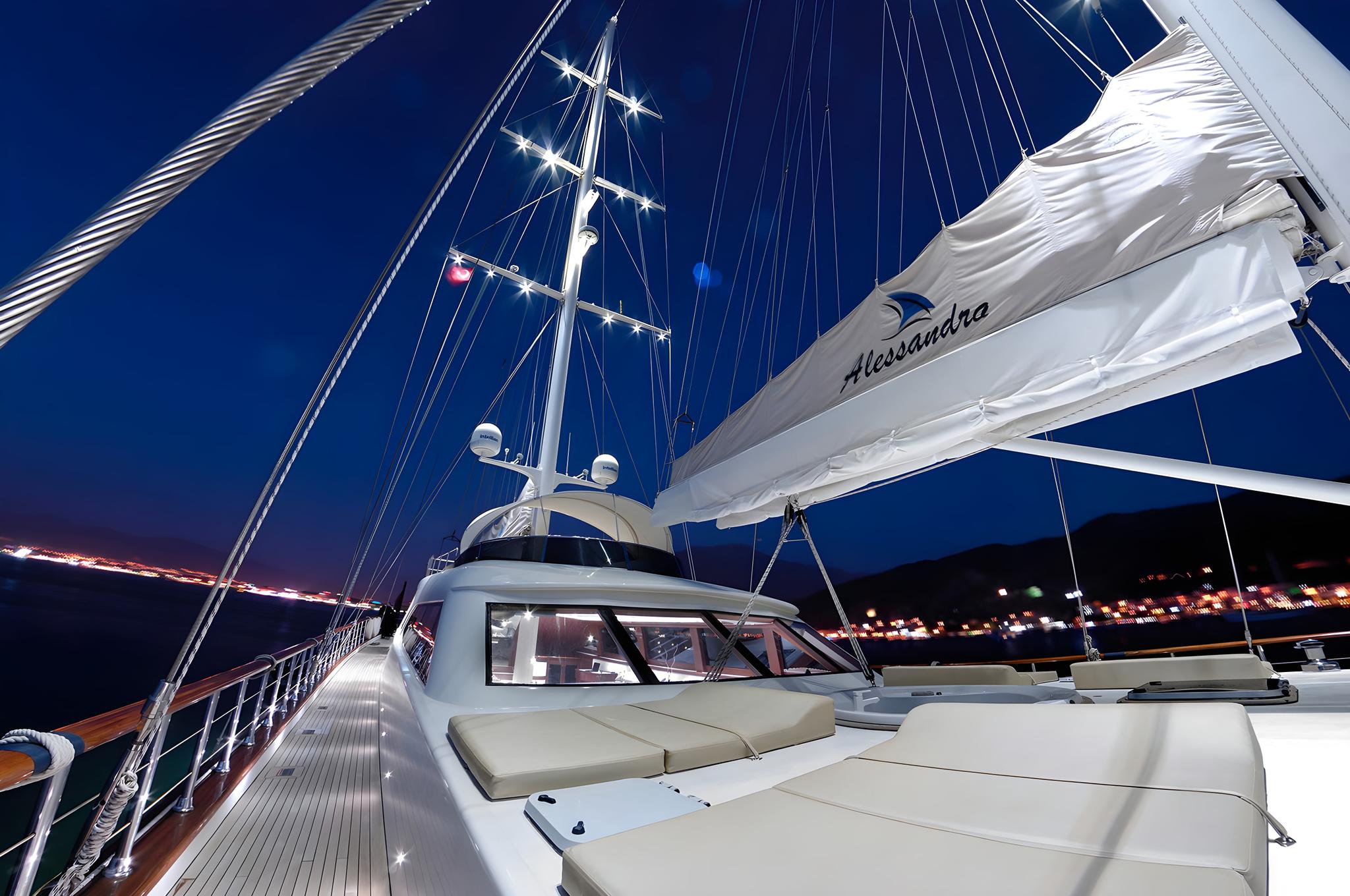 yacht bow deck with white cushioned seating area and mast rigging at night