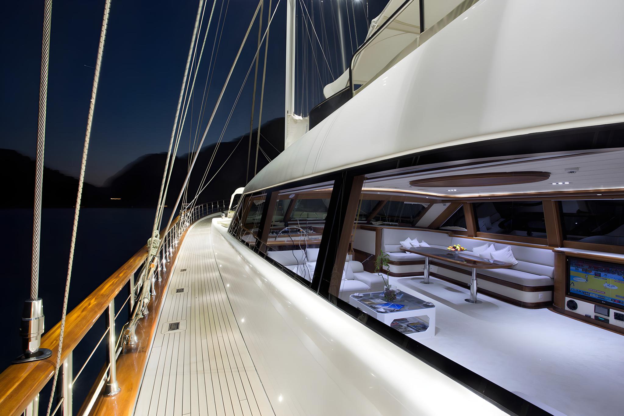 gulet side deck with teak walkway and illuminated salon lounge seating at twilight