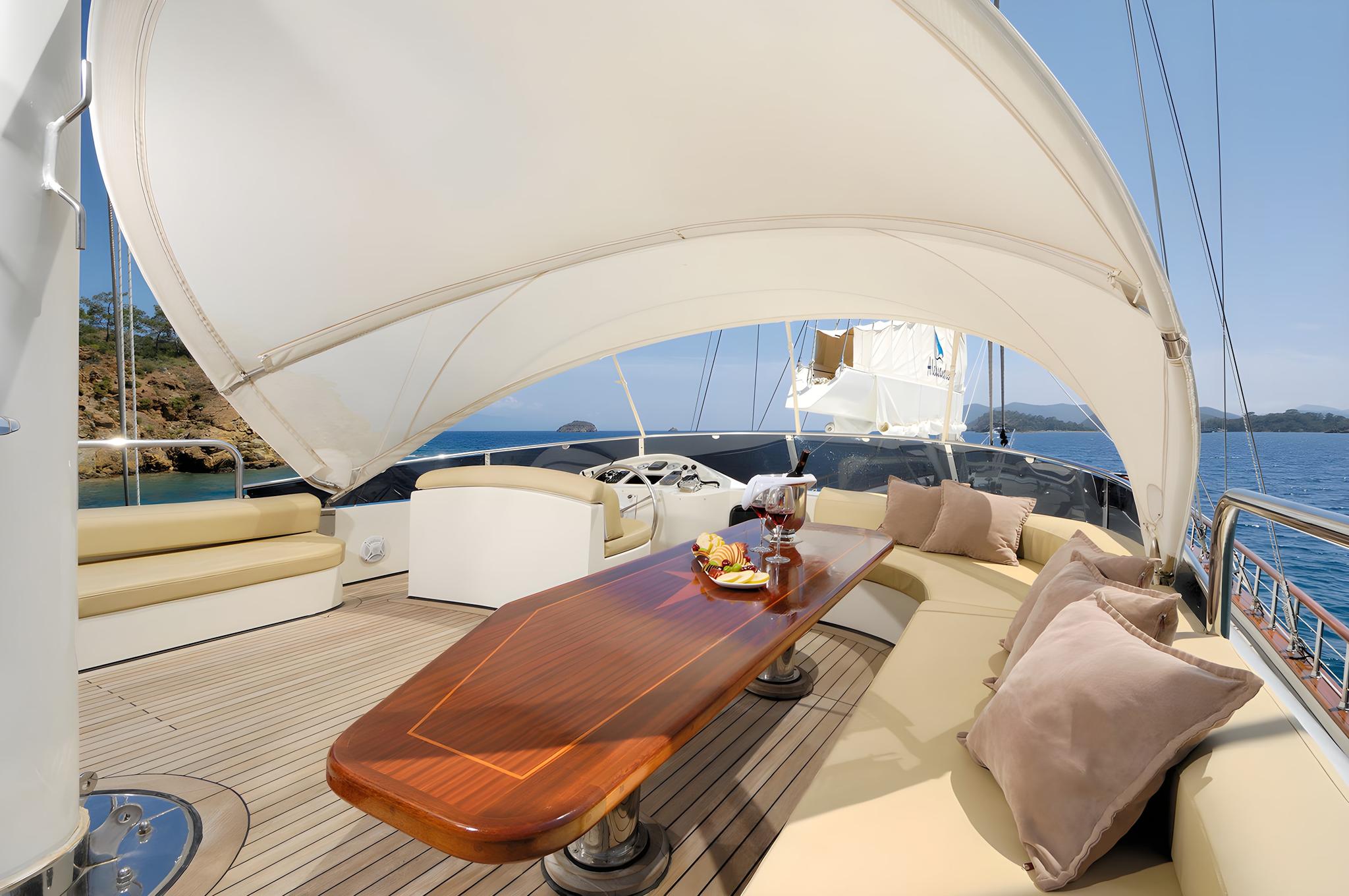yacht aft deck with curved banquette seating, polished wood dining table under fabric canopy