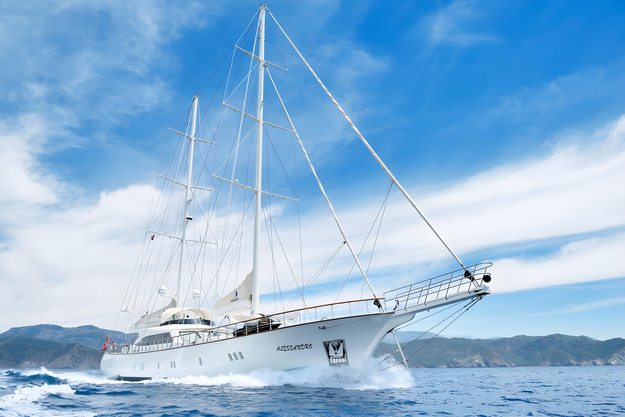 white luxury sailing yacht Alessandro underway with three masts and mountainous coastline