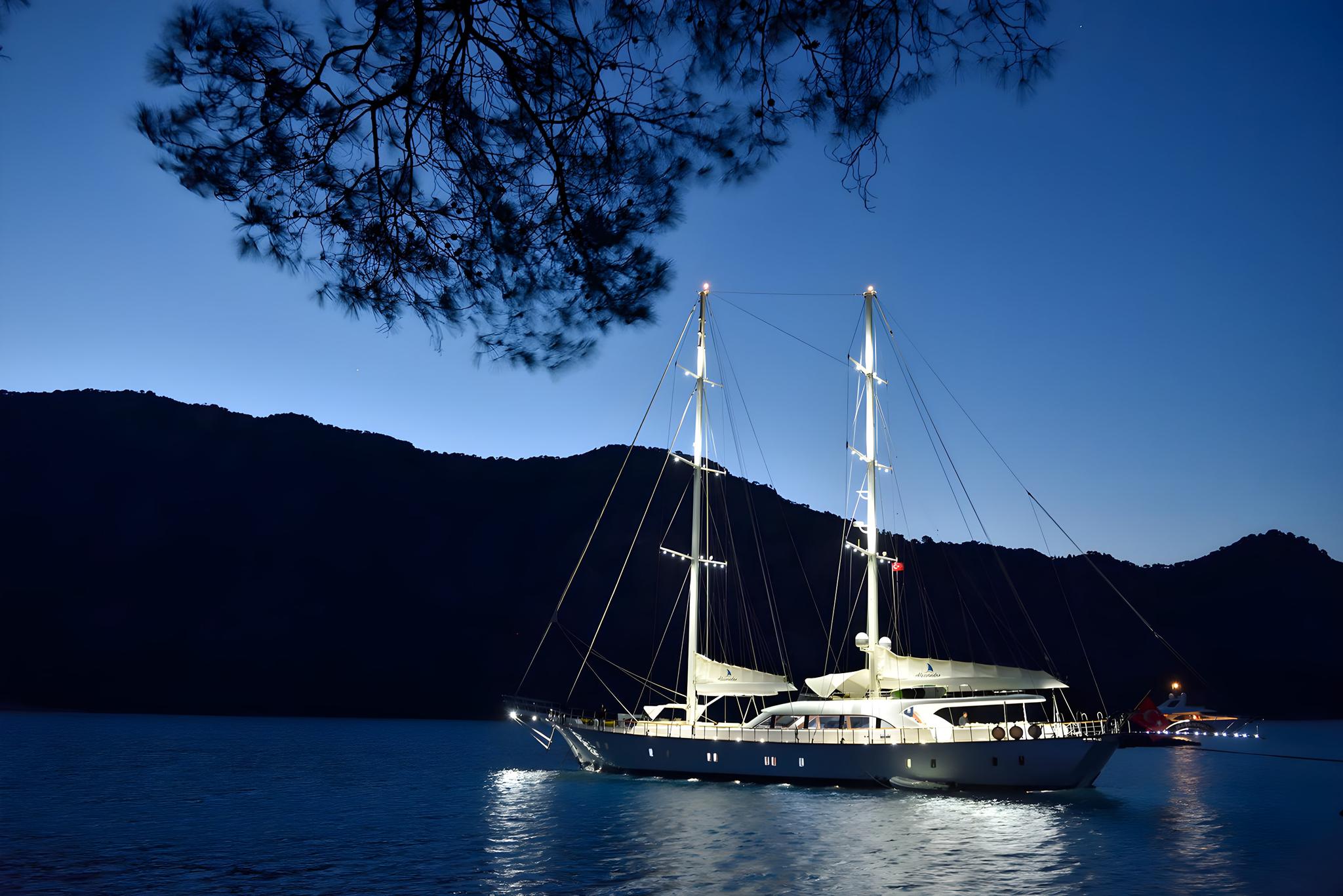 luxury white gulet anchored in calm bay at twilight with illuminated masts and hills