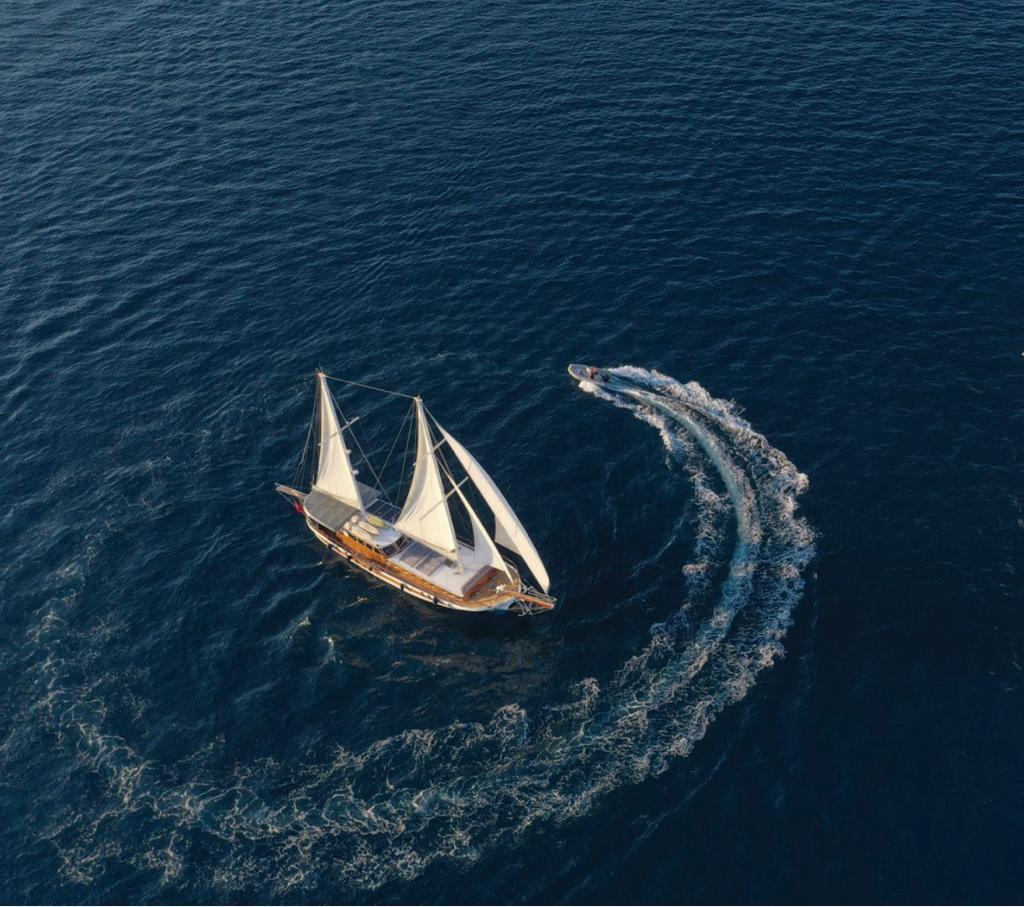 aerial drone shot of traditional wooden gulet with white sails navigating deep blue waters