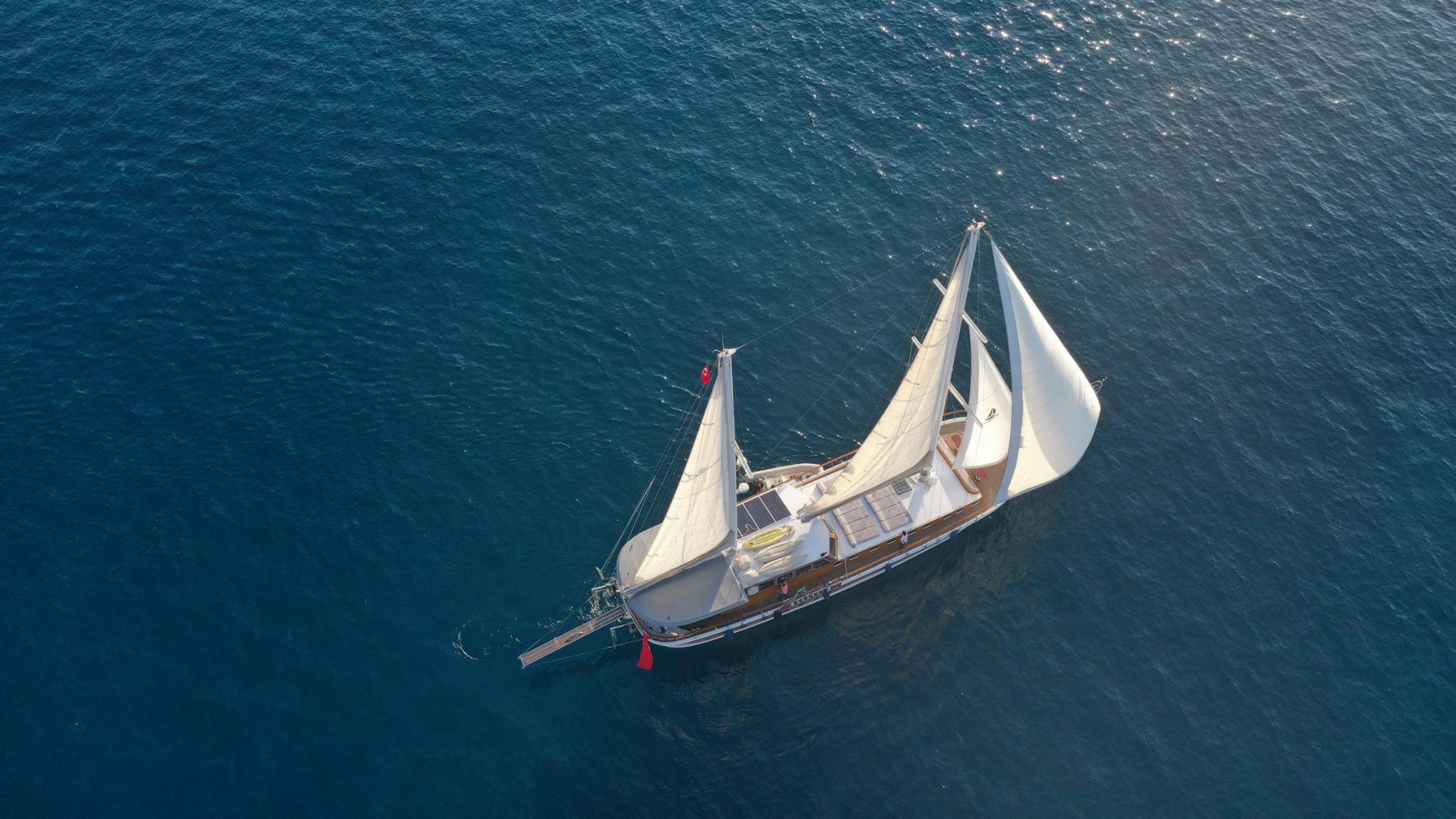 aerial view of traditional white gulet with raised sails anchored in deep blue water
