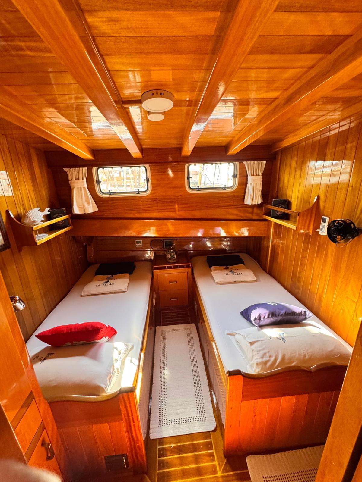 guest cabin interior with twin beds, wood paneling, portholes and storage compartments