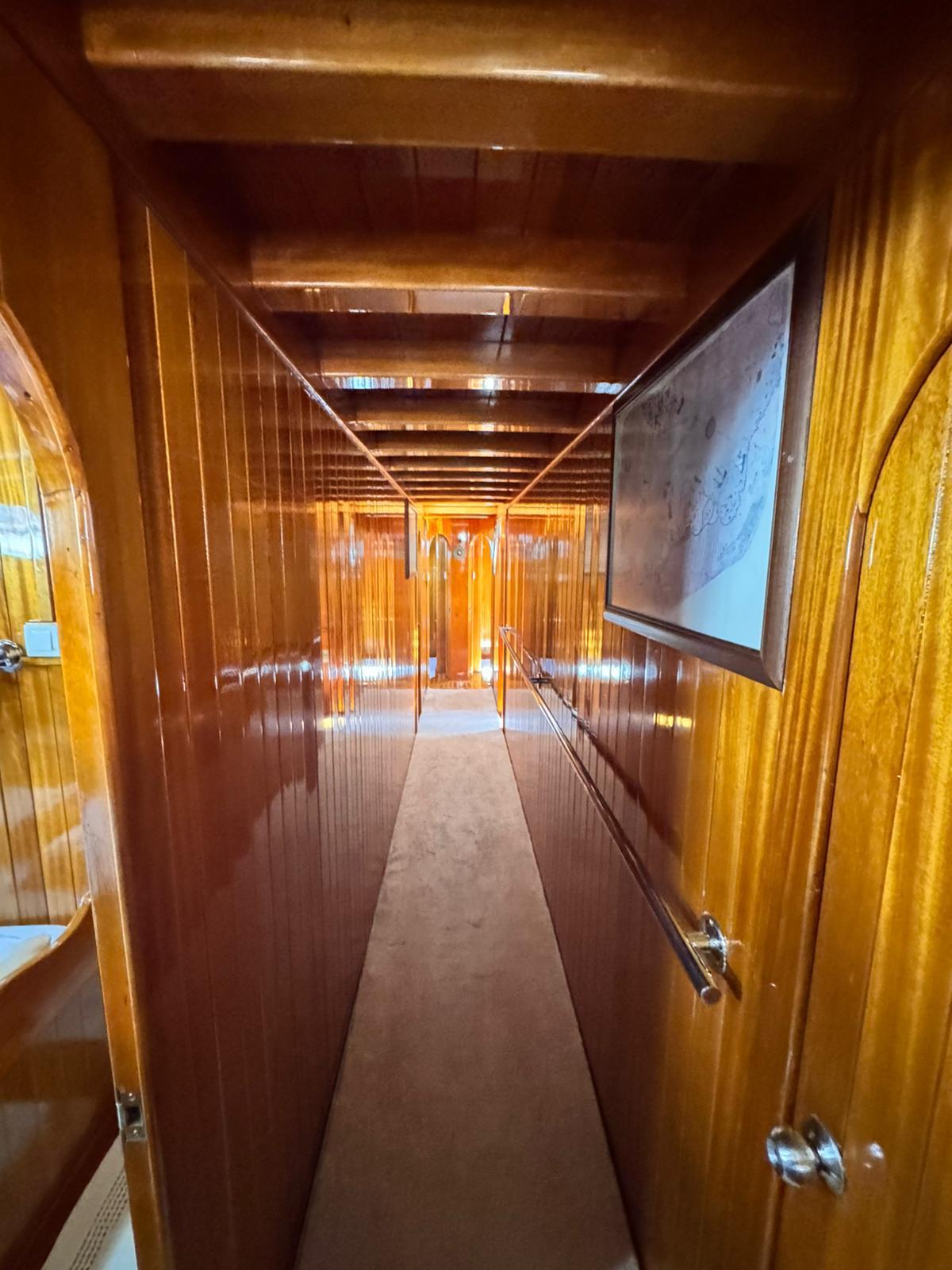 yacht interior corridor with polished wood paneling, exposed ceiling beams, and cabin doors