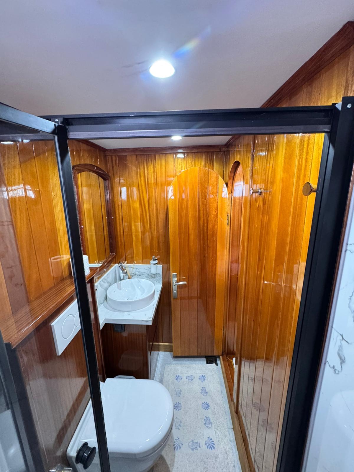 yacht bathroom interior with white toilet, round sink, and warm wood paneling
