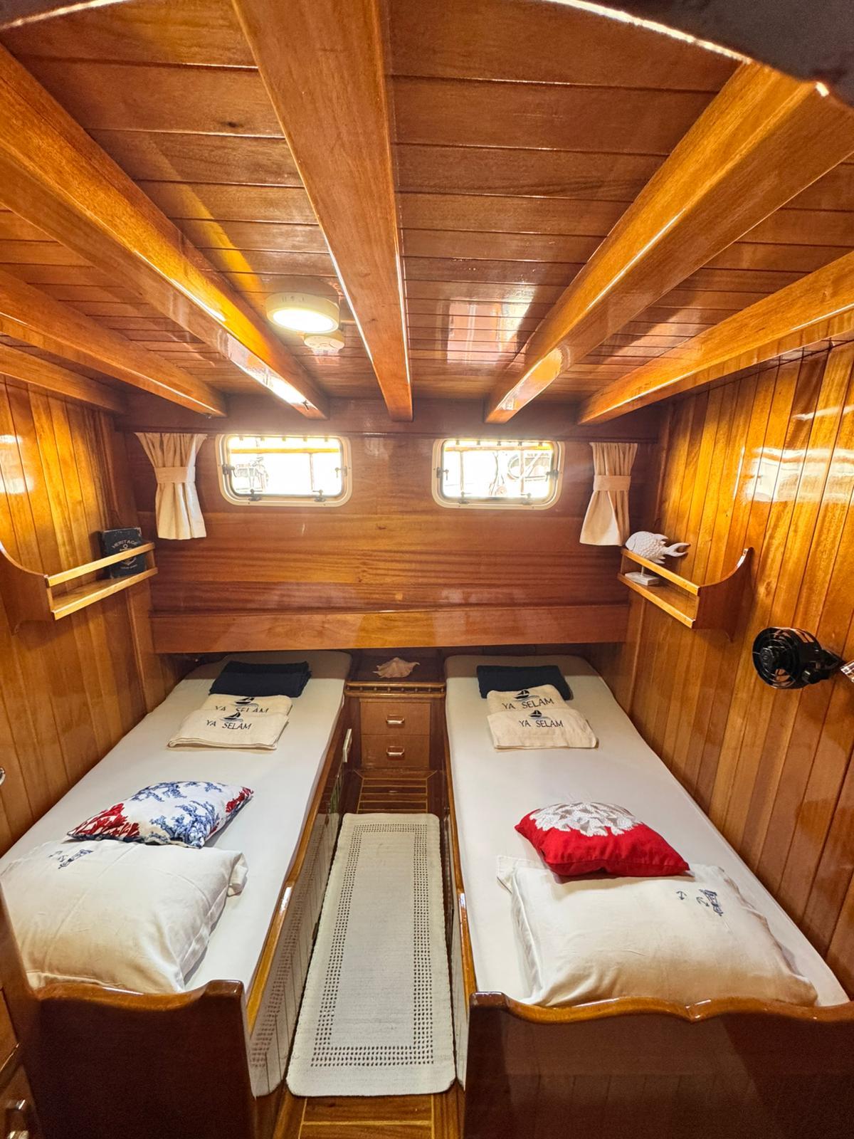 twin cabin with two single beds, wooden paneling, portholes with curtains and built-in storage