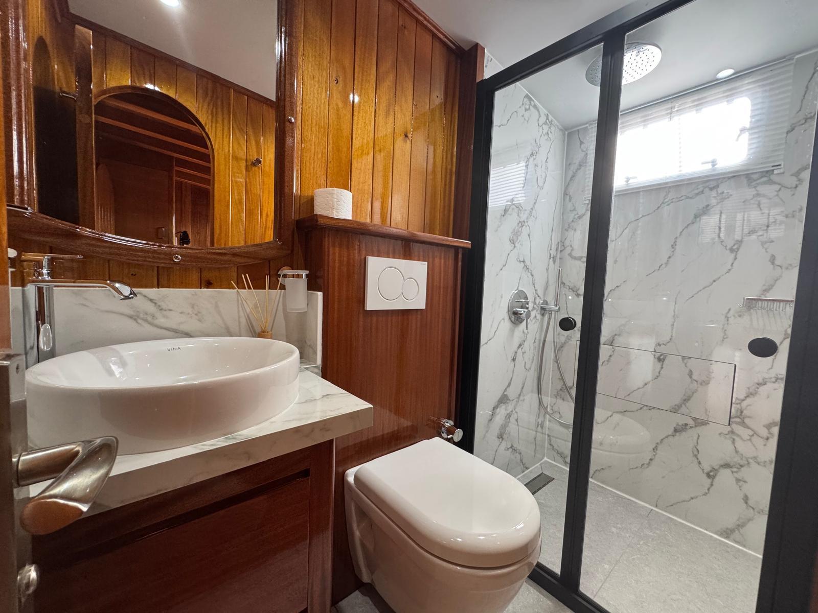 yacht bathroom featuring white vessel basin, wooden cabinetry, and marble-tiled shower enclosure