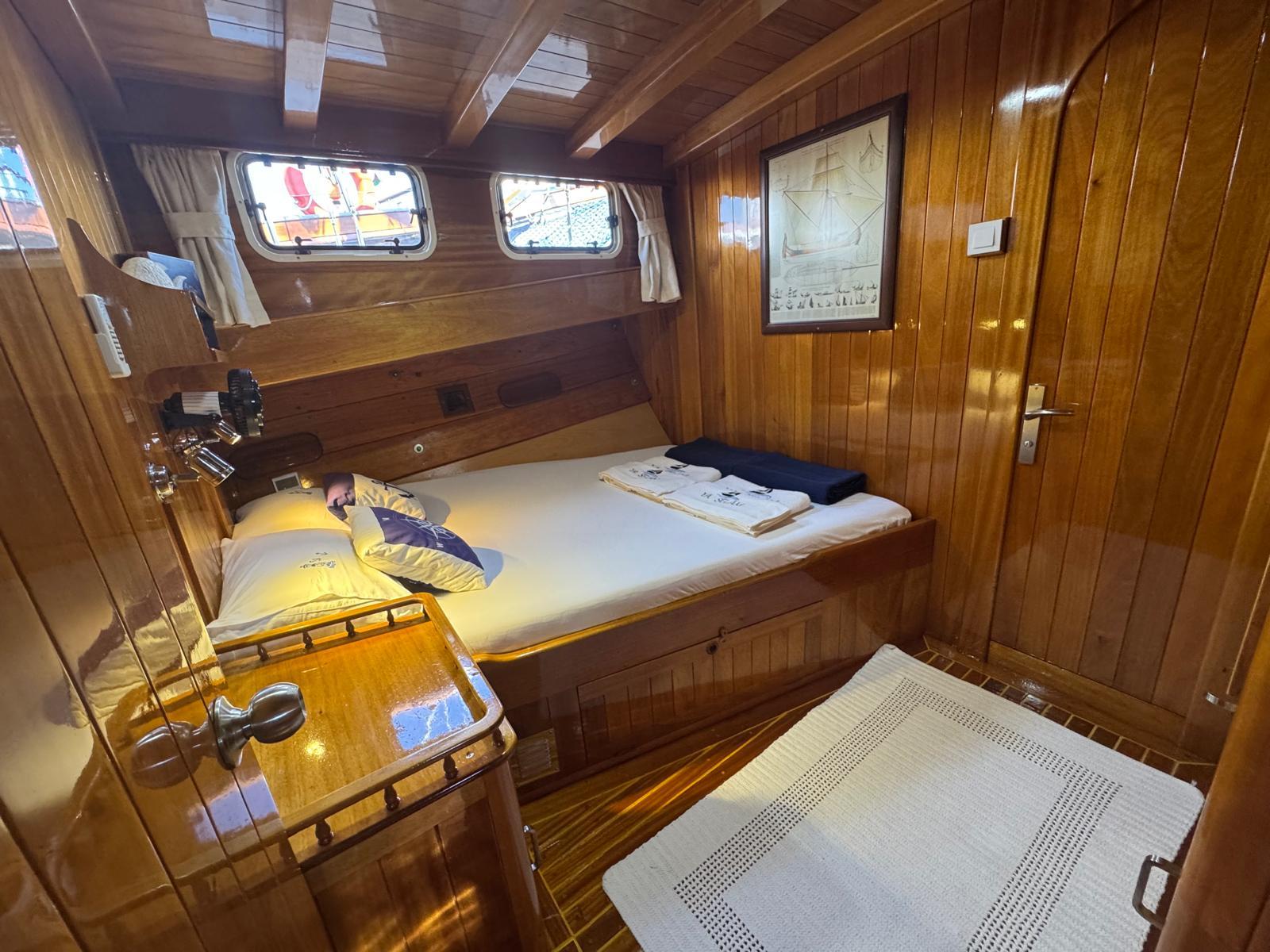 yacht guest cabin featuring double bed, wooden paneling, portholes, and nautical chart artwork
