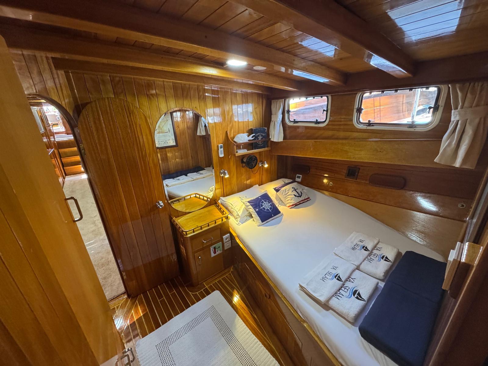 yacht guest cabin featuring single bed with white linens, wooden paneling, porthole windows and nautical decor