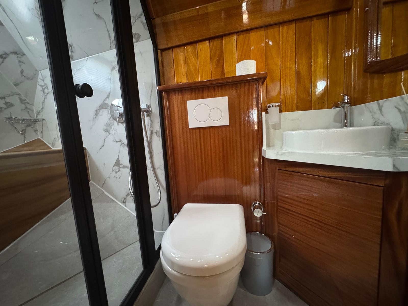 yacht bathroom featuring white toilet, vessel sink, marble walls, and glass shower enclosure