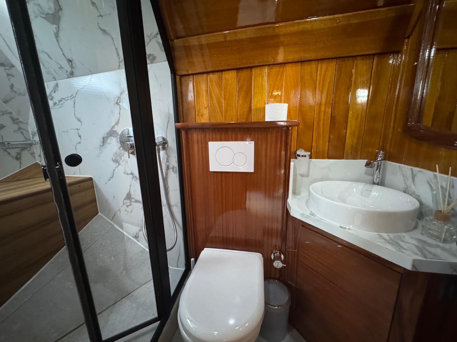 yacht bathroom featuring white toilet, marble vanity with round sink and glass shower door