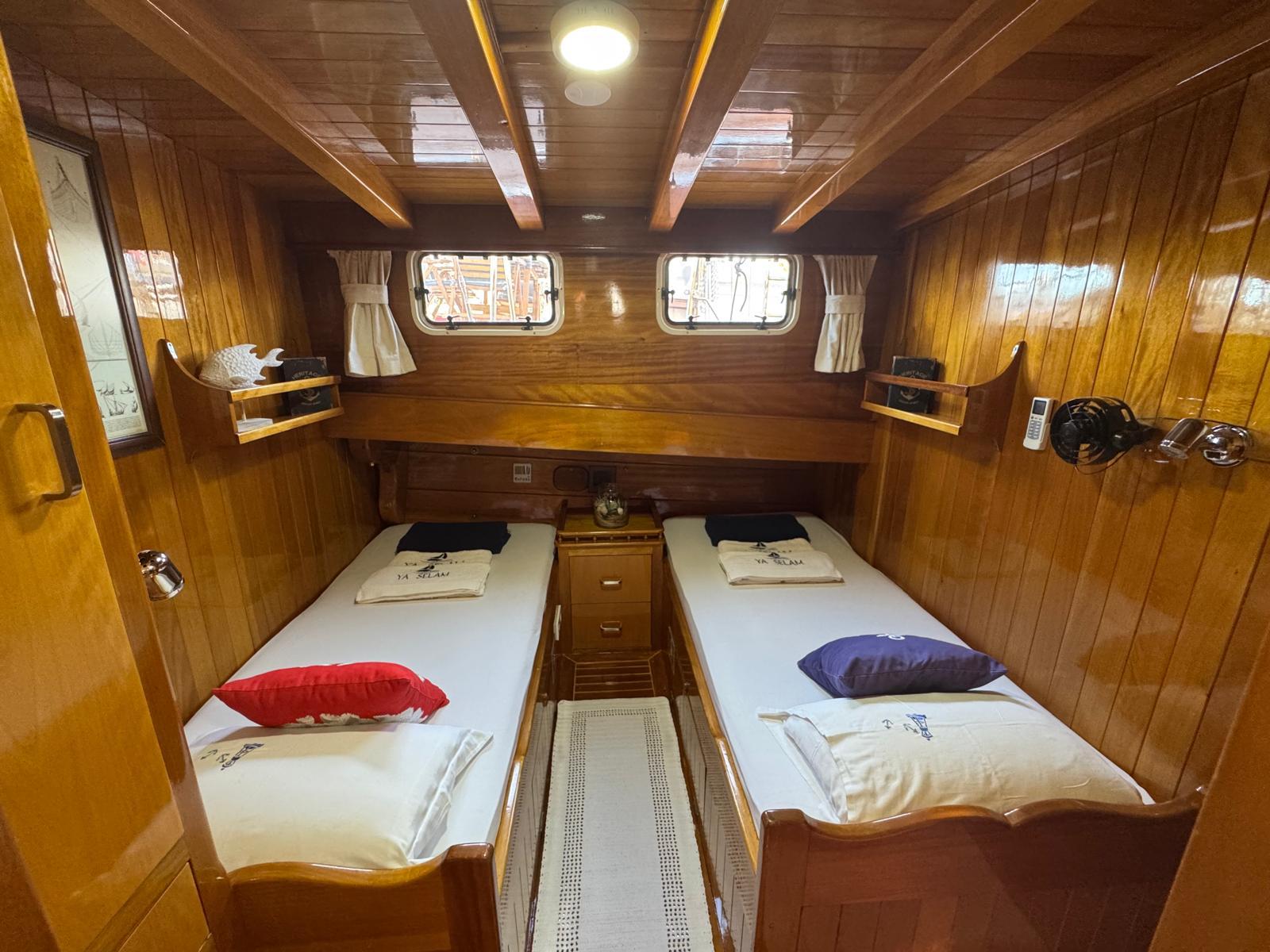 yacht twin cabin with two single beds, wooden walls, portholes and storage compartments