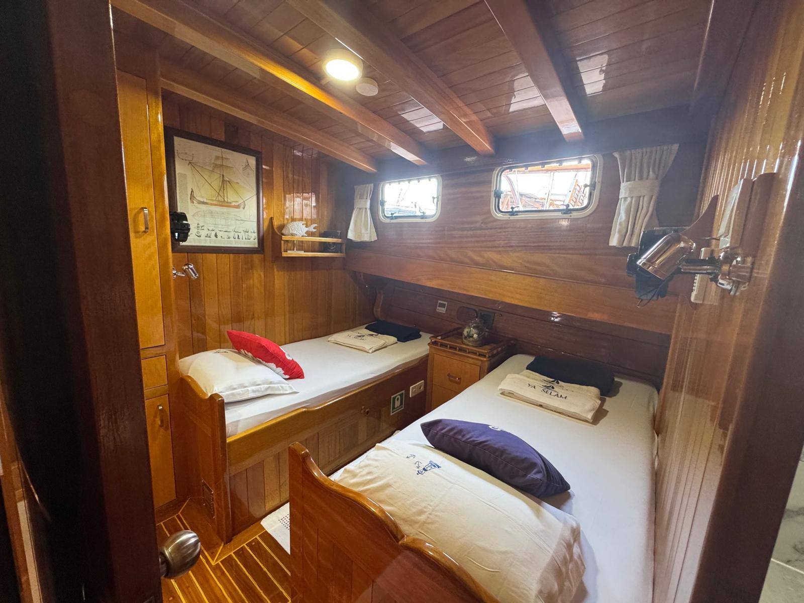 yacht twin cabin with two single beds, wooden paneling, portholes and nautical artwork