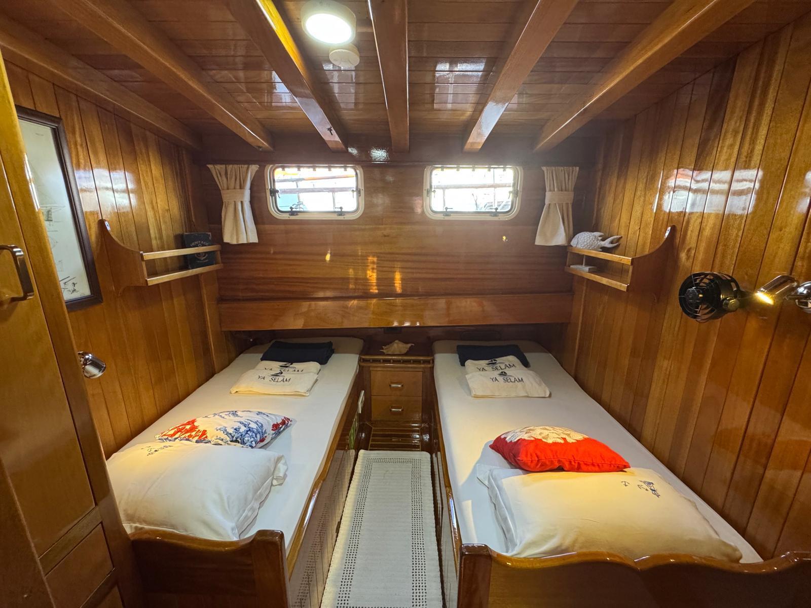 Twin cabin interior with two single beds, wooden walls, portholes and central nightstand