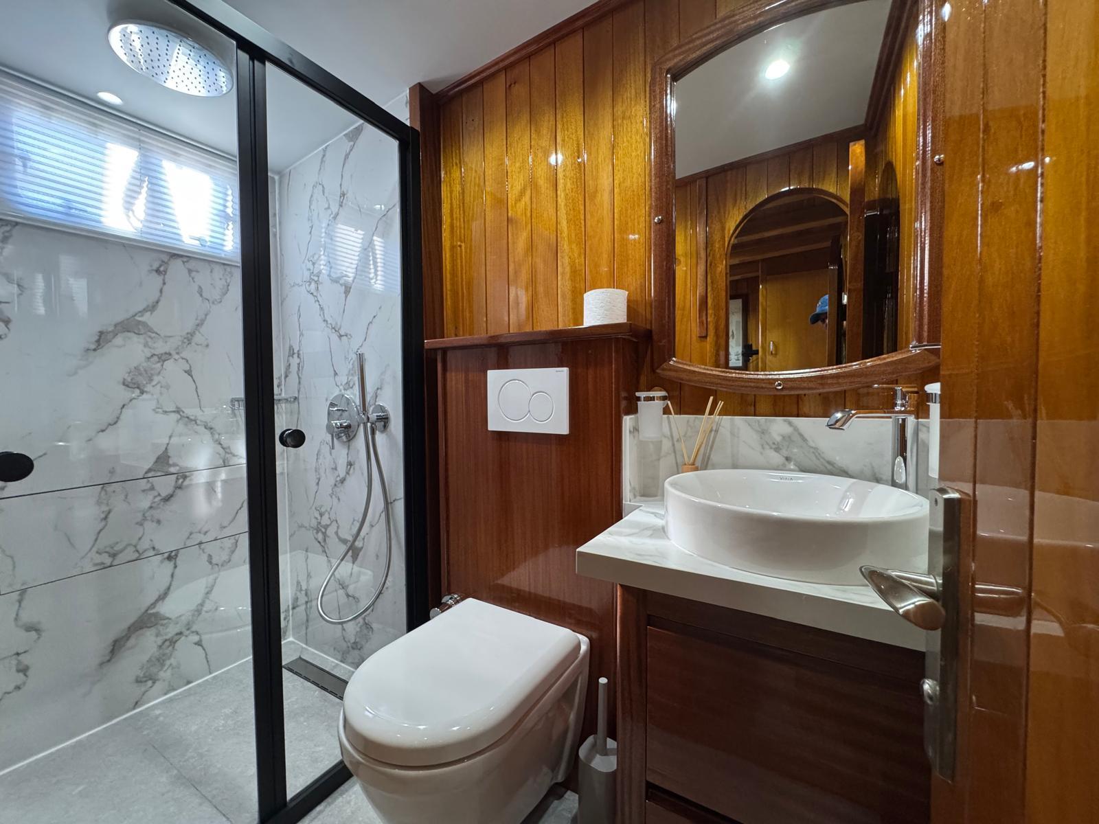 yacht bathroom with marble shower, round basin, mirror and wooden paneling