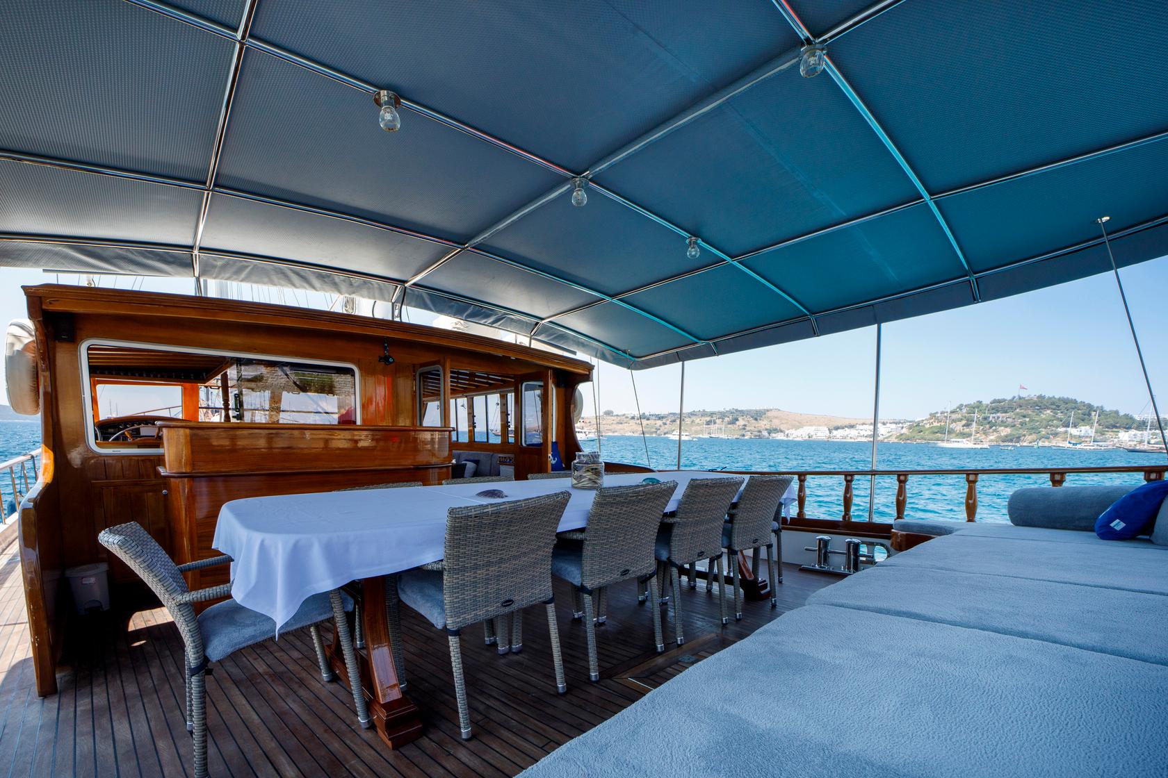 Gulet aft deck dining area with wicker chairs, white tablecloth and coastal views