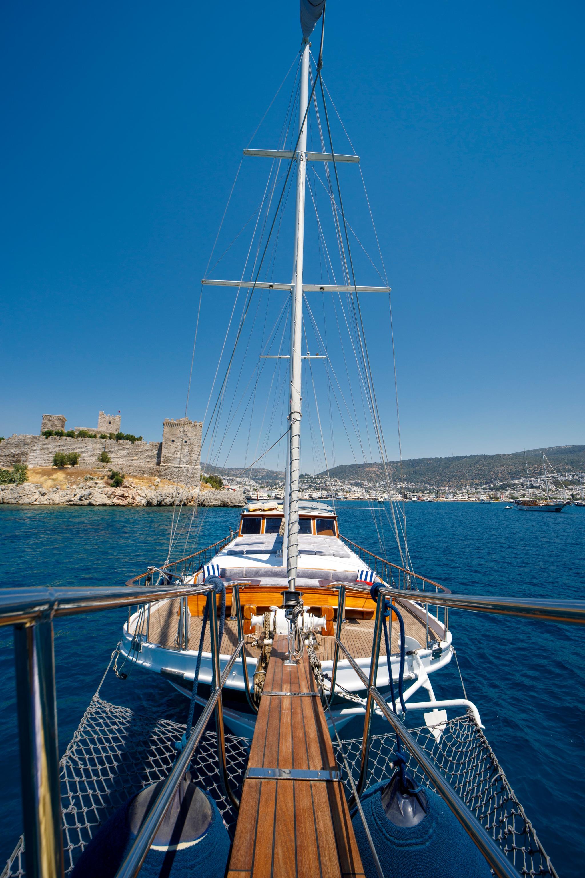 traditional gulet bow deck showing wooden planking, central mast with rigging and Mediterranean coastline