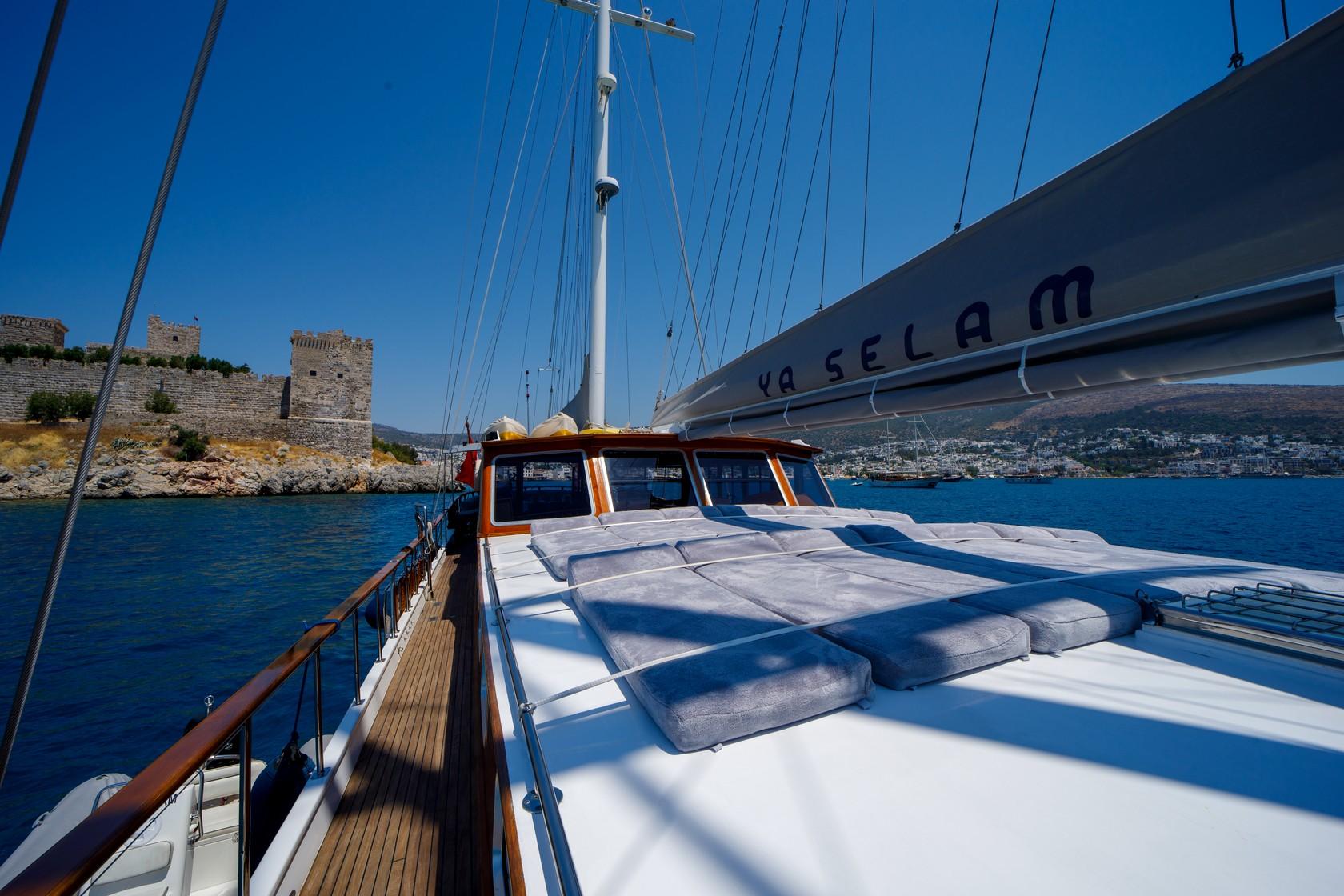 gulet bow deck featuring white sun cushions and wooden wheelhouse with coastal backdrop