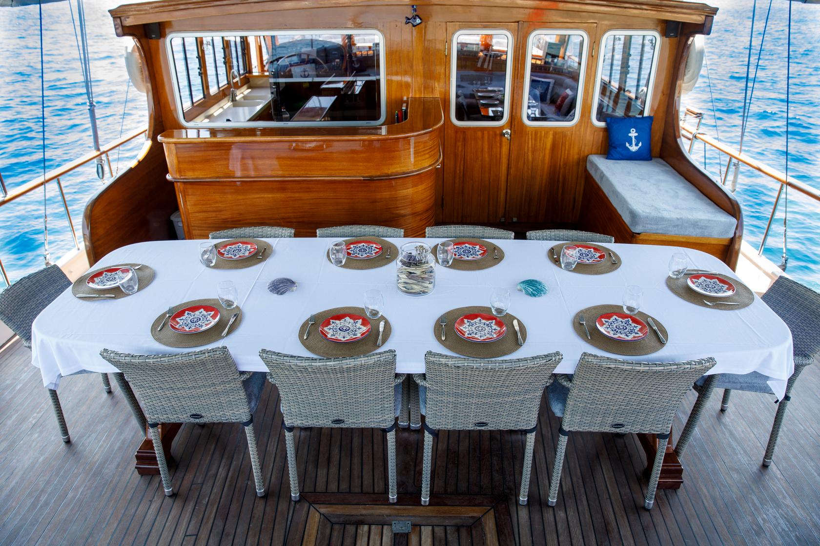 Yacht aft deck dining area with oval table set for ten guests and wheelhouse