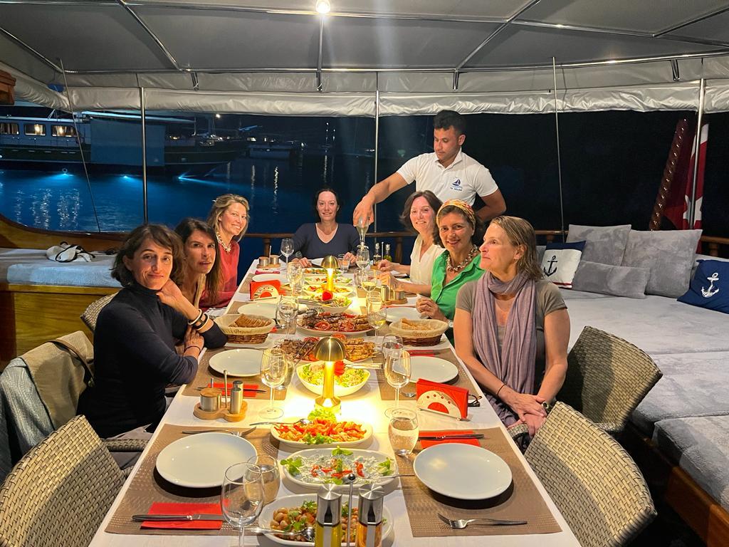 guests enjoying dinner with served food and wine on yacht's covered aft deck at night
