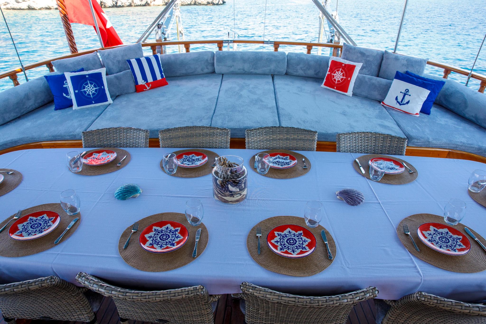 yacht aft deck with curved blue seating, formal dining table setting and nautical cushions