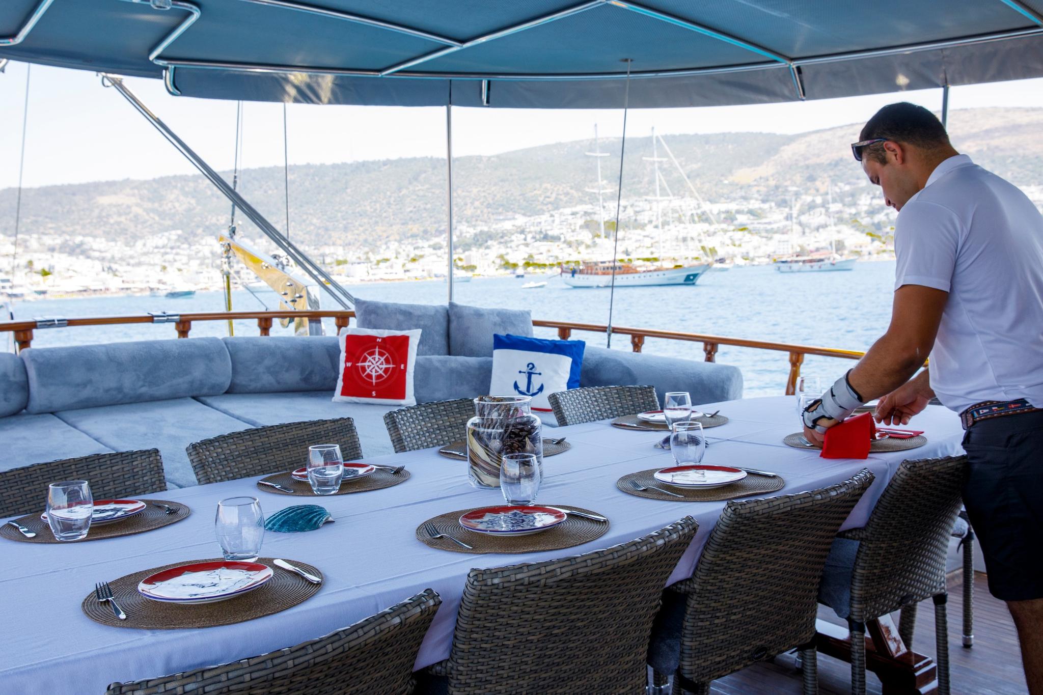 crew member arranging place settings on white outdoor dining table with nautical cushions