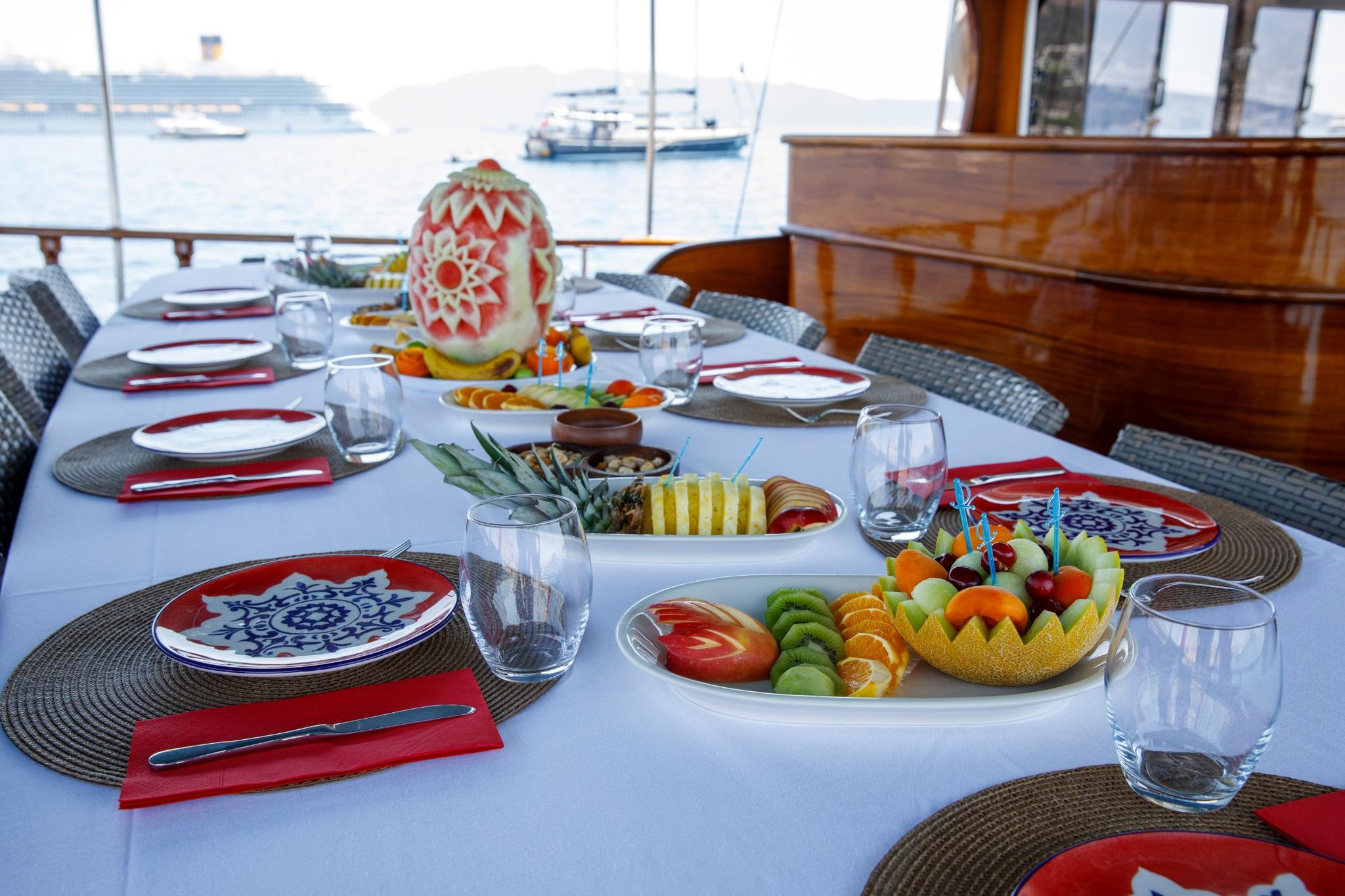 yacht dining table with ornate watermelon carving, fresh fruit platters and formal place settings
