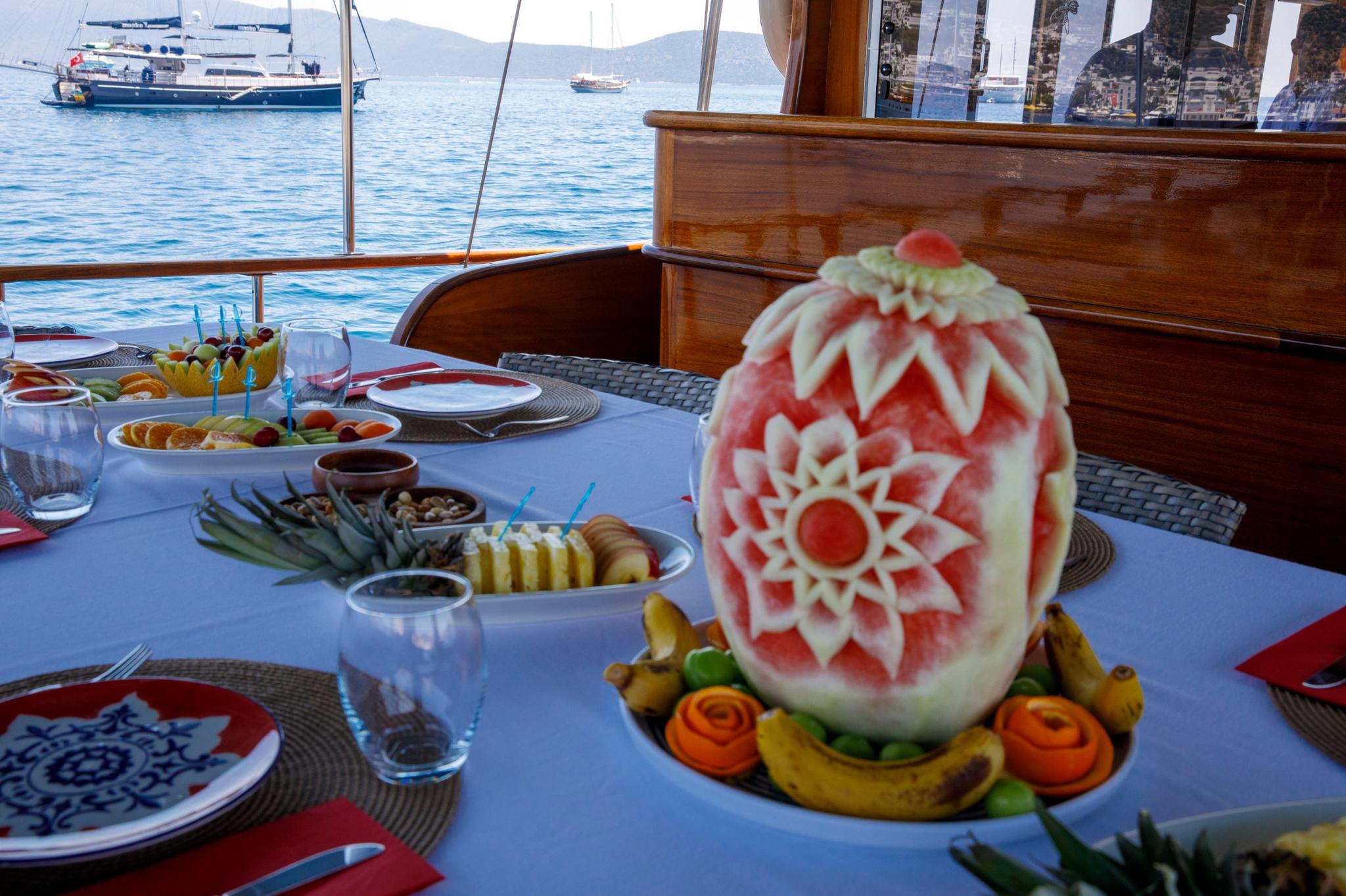 yacht dining table featuring ornate carved watermelon centerpiece with fruit platters and place settings