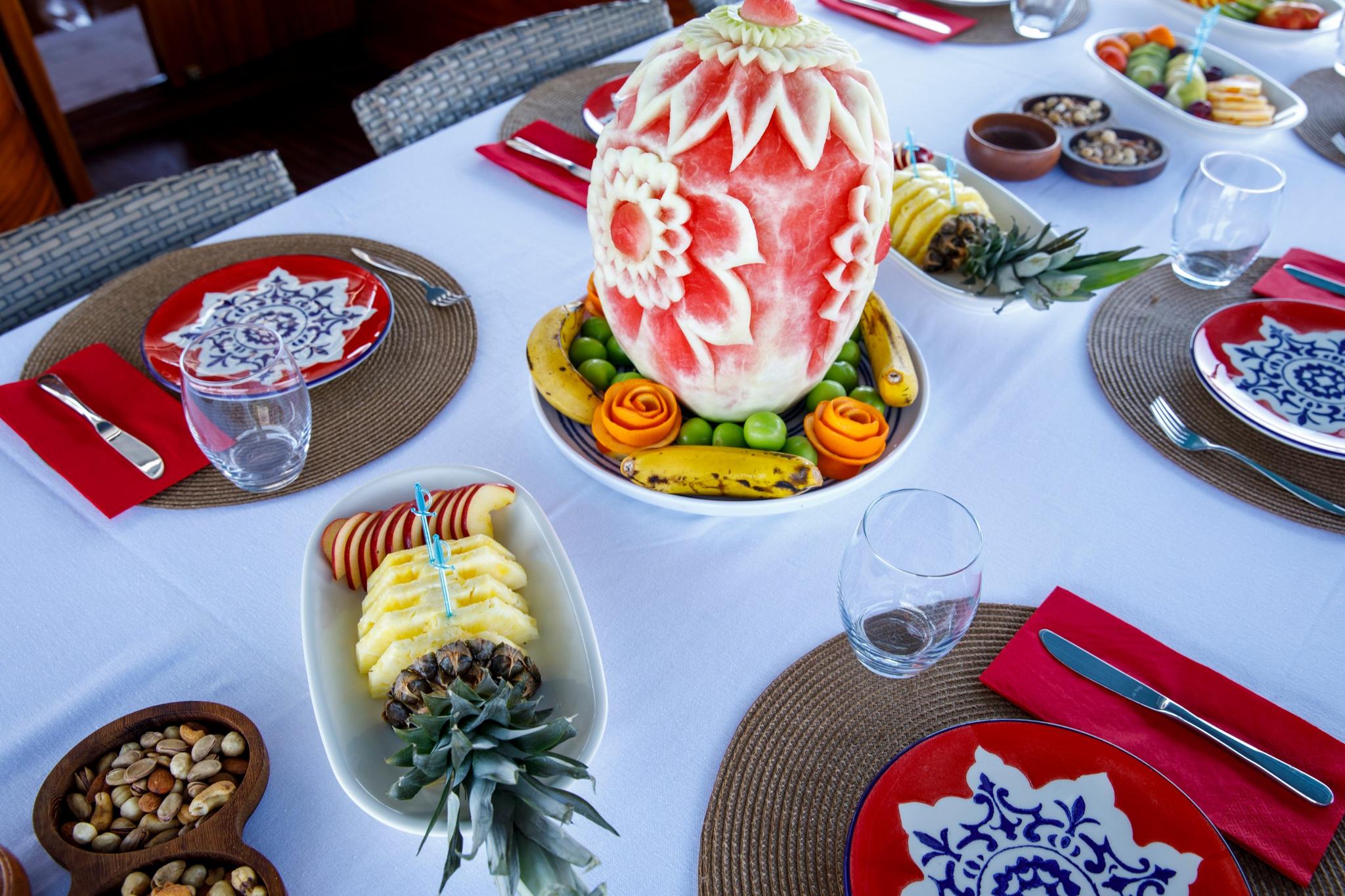 Yacht dining table with carved watermelon centerpiece, fresh fruit platter and formal place settings