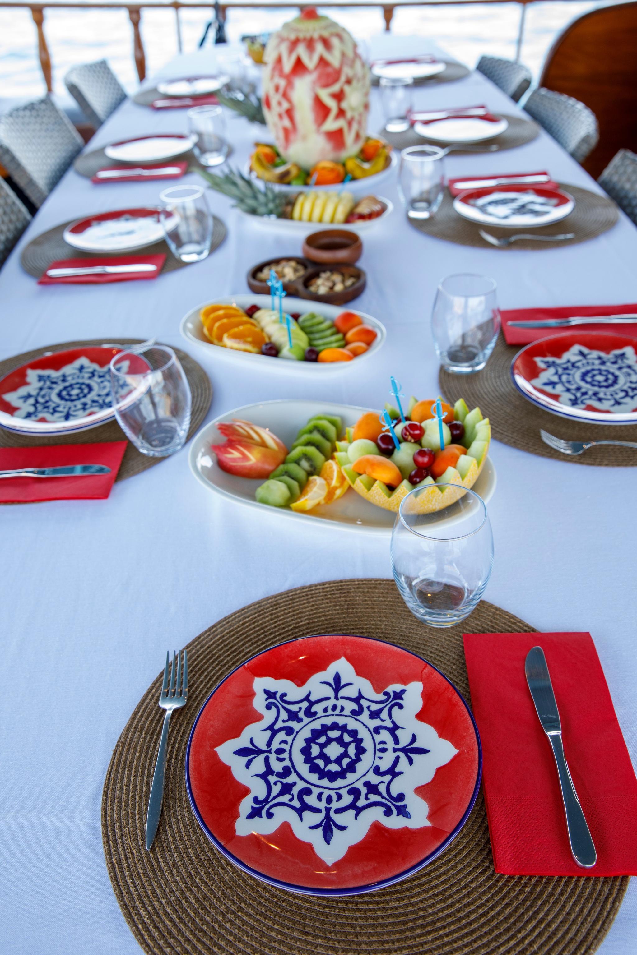 Elegant yacht dining table with ornate plates, carved watermelon centerpiece and fresh fruit platters