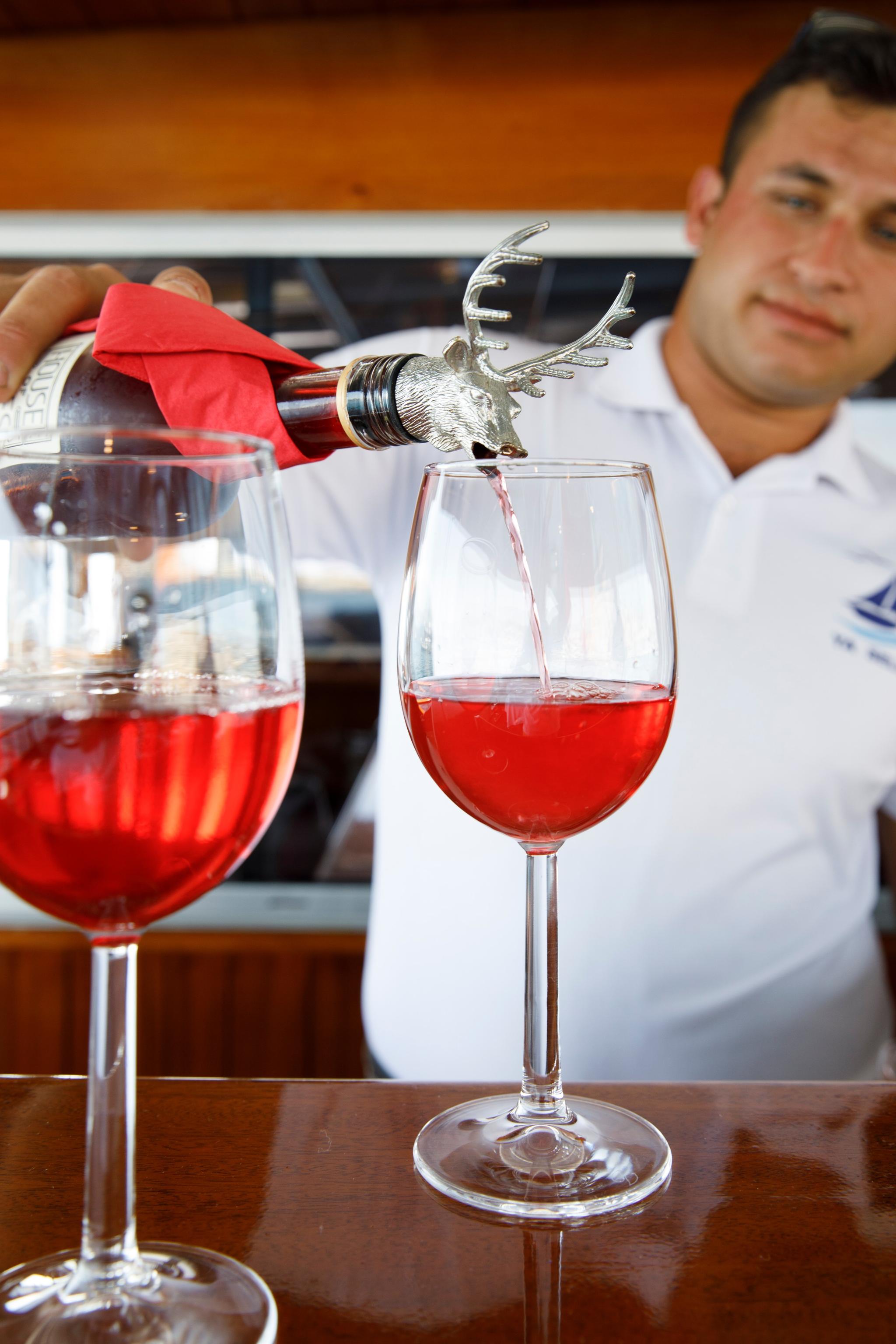 yacht crew member pouring red wine from decorative bottle into wine glass onboard