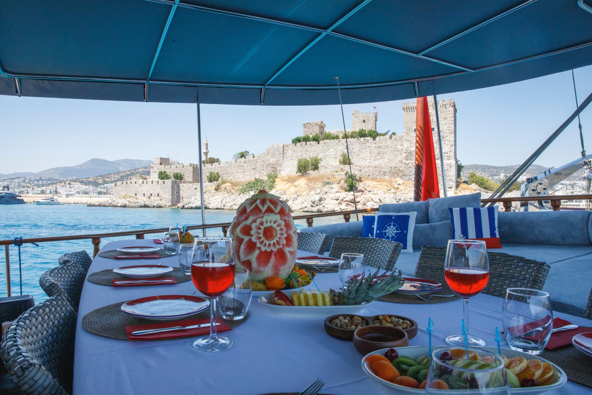 Aft deck dining table with red wine glasses and Mediterranean appetizers overlooking historic castle