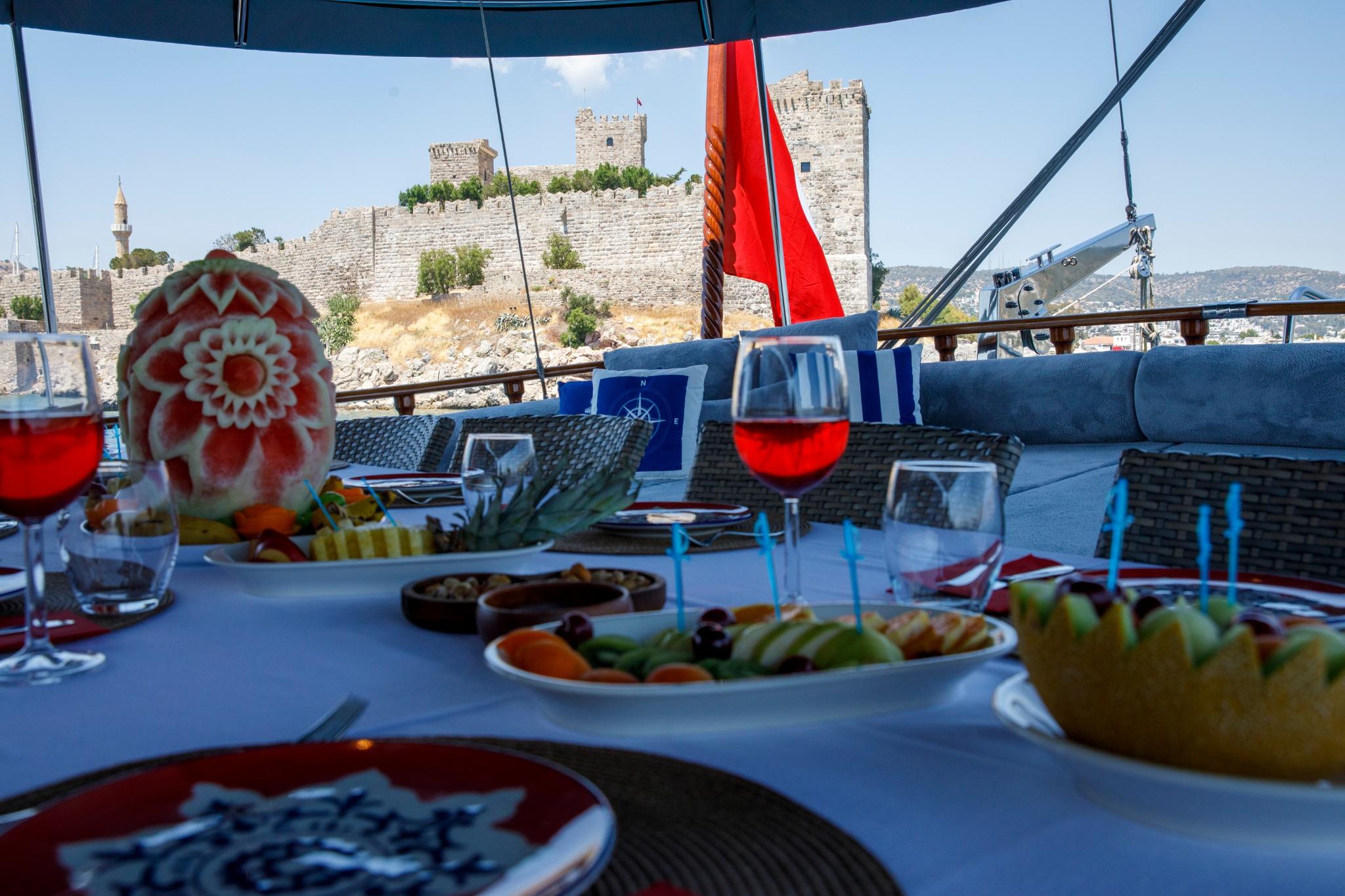 yacht dining table with served meals, wine glasses and historic castle backdrop