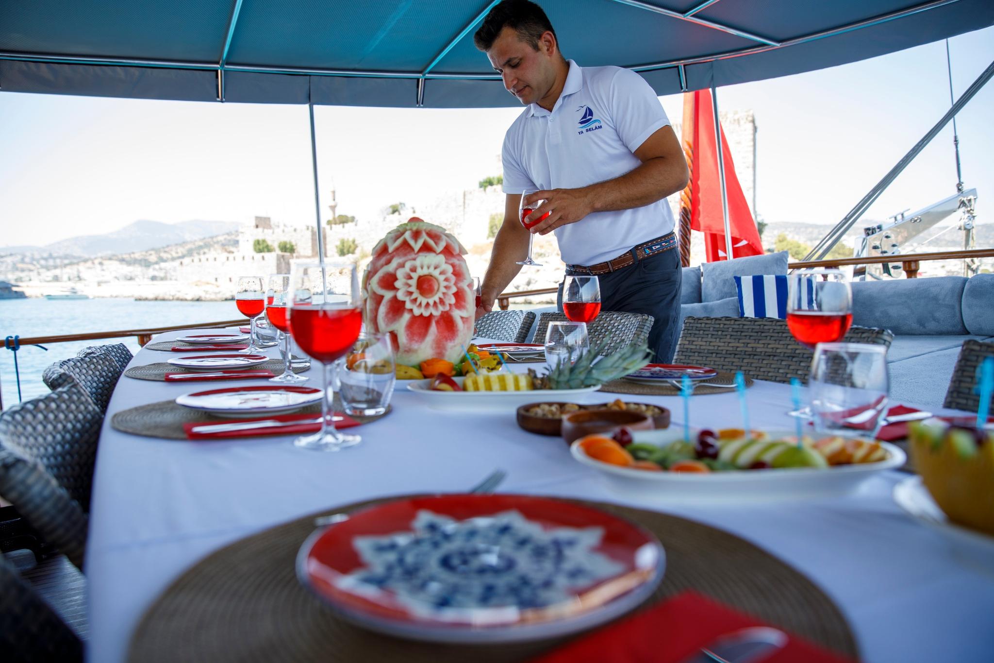 crew member in white polo shirt serving red drinks at yacht dining table with food plates