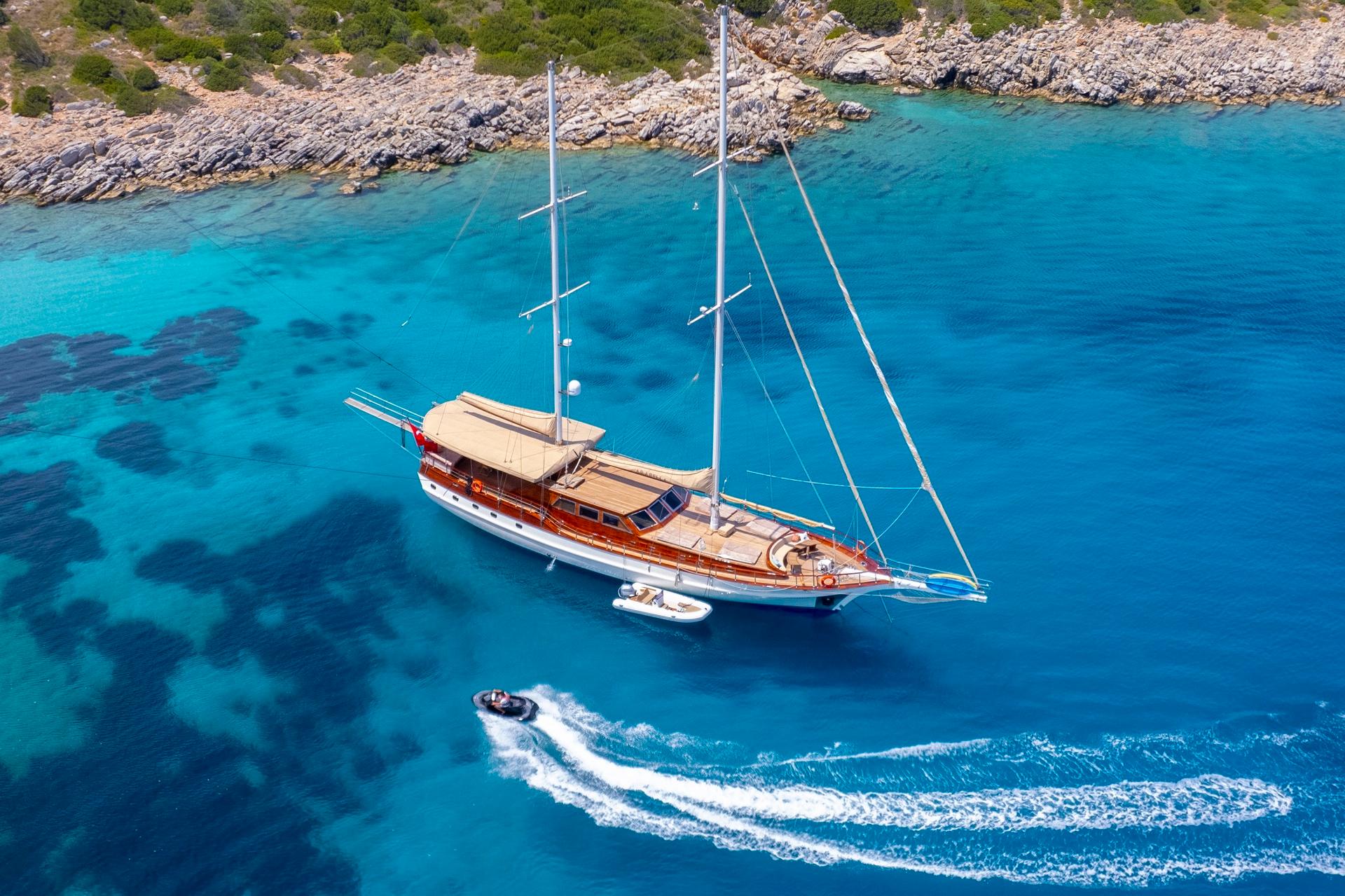 aerial view of wooden gulet yacht anchored in crystal clear turquoise bay with tender boat