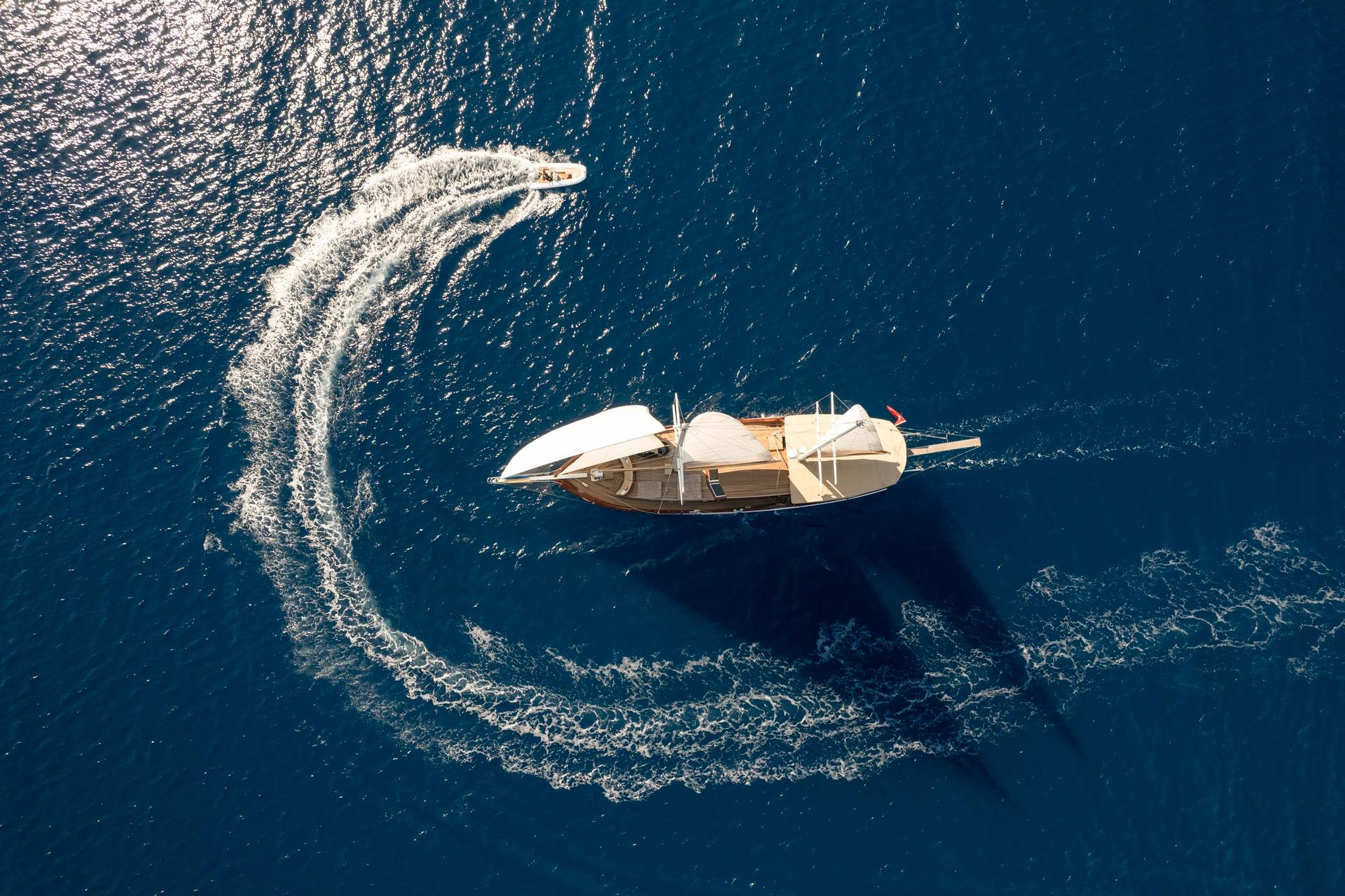aerial view of traditional gulet yacht at anchor with tender boat circling and creating white water wake
